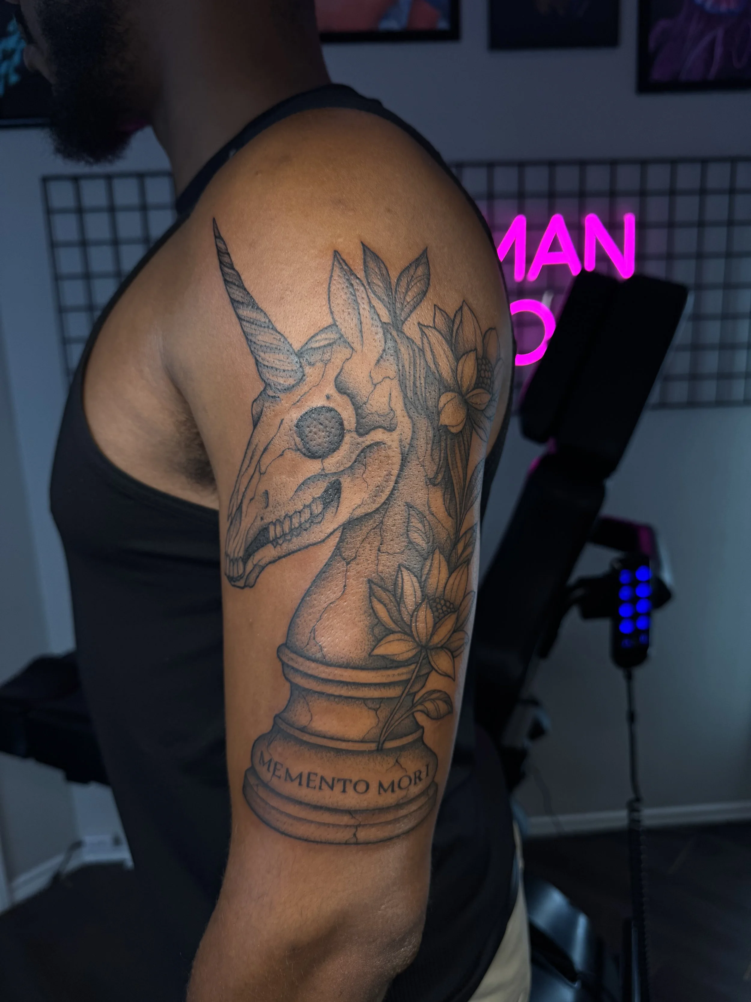 Tattoo of a unicorn skull with flowers on the person's upper arm.