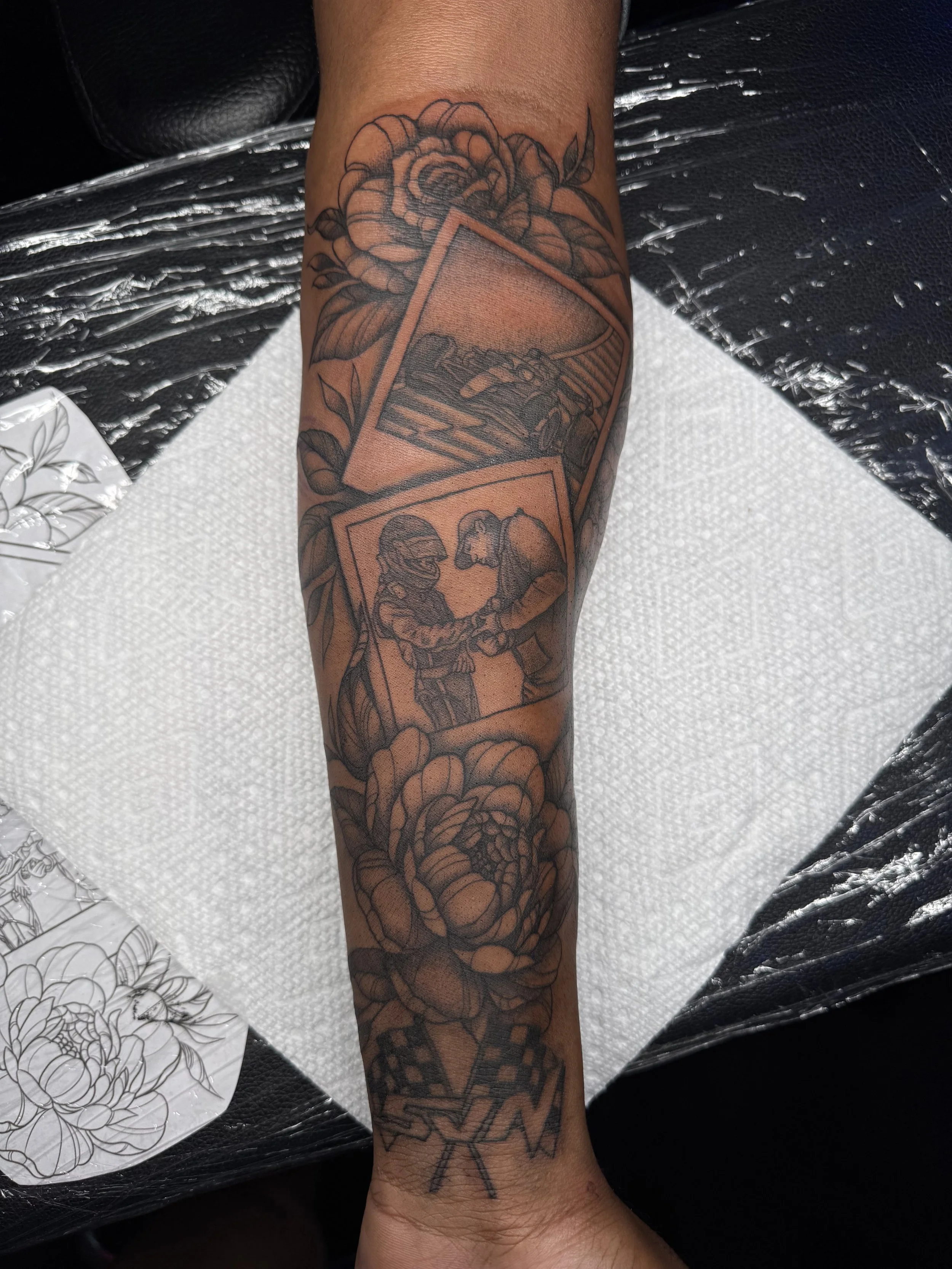 Tattoo of a grandmother and grandson holding hands inside a frame, with large roses surrounding the images, on a person's forearm.