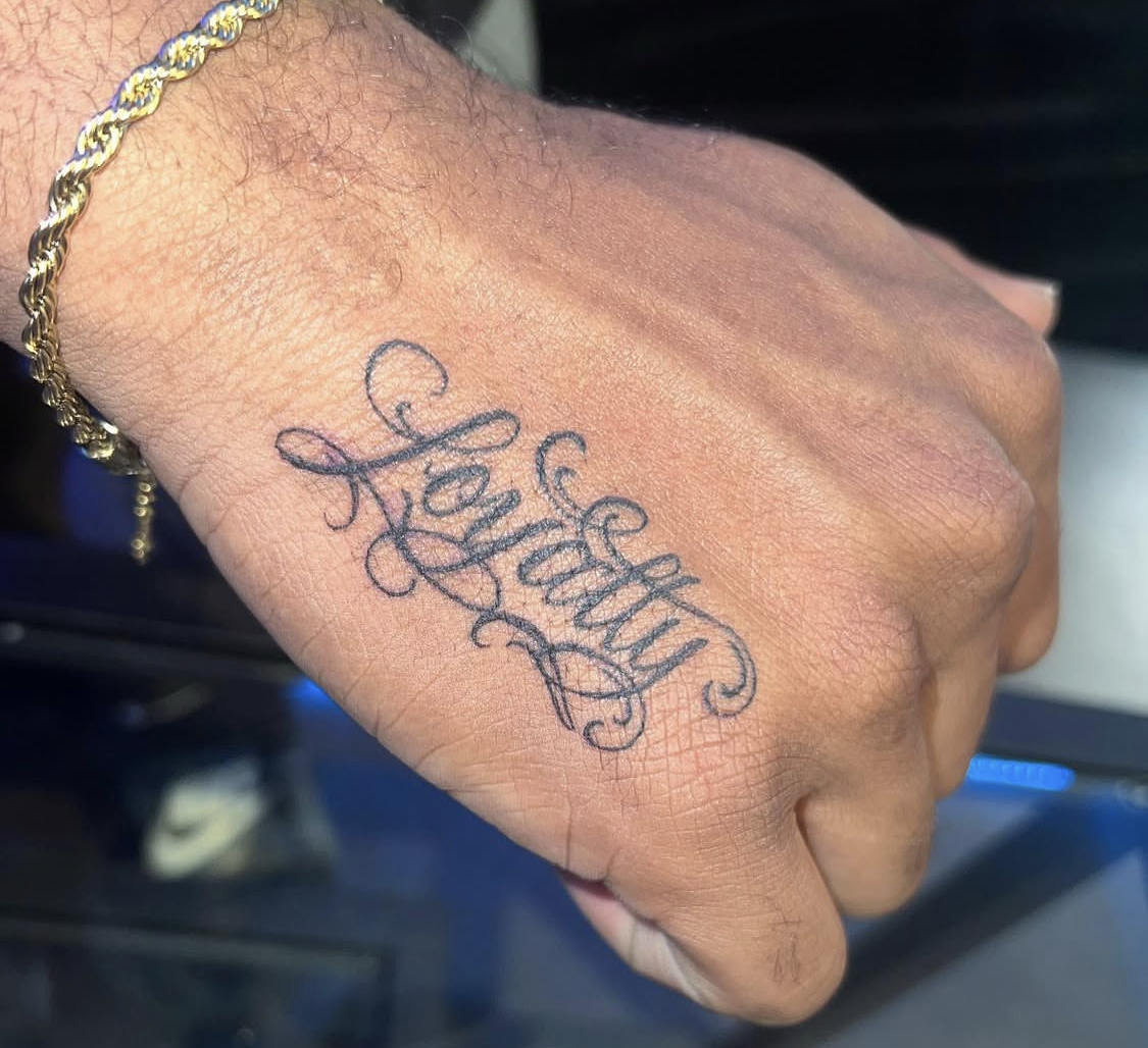 Tattoo on hand that says 'Love Yourself' in cursive script.