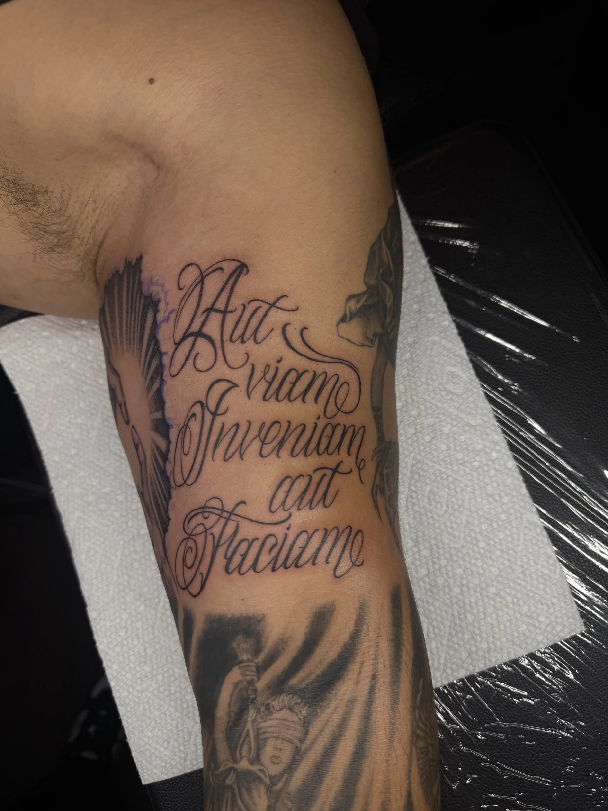 Tattoo on person's arm with Latin quote and religious imagery.