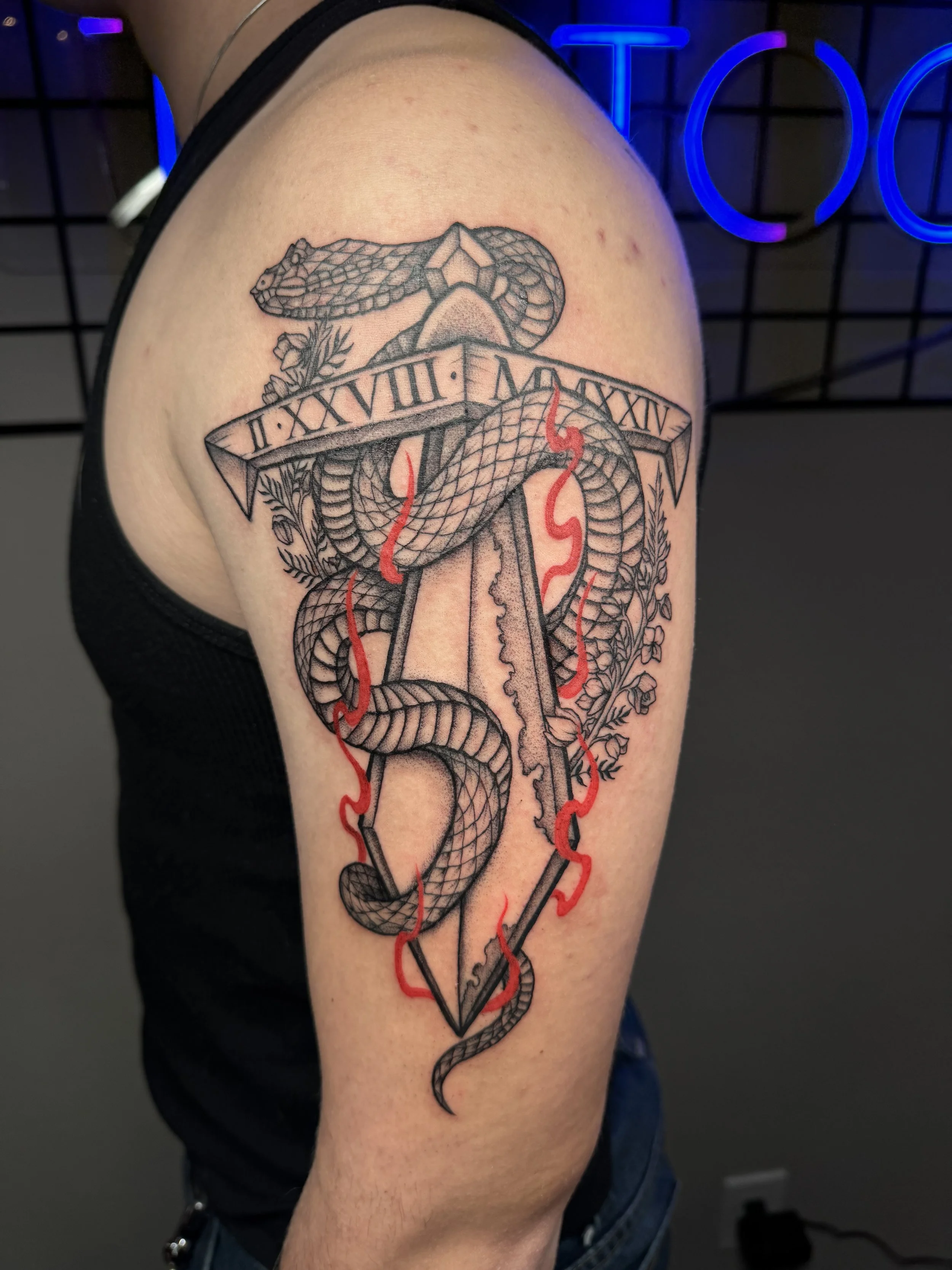 Tattoo of a snake intertwined with a dagger, with a banner containing Roman numerals, and red flames around the dagger on a person's upper arm.