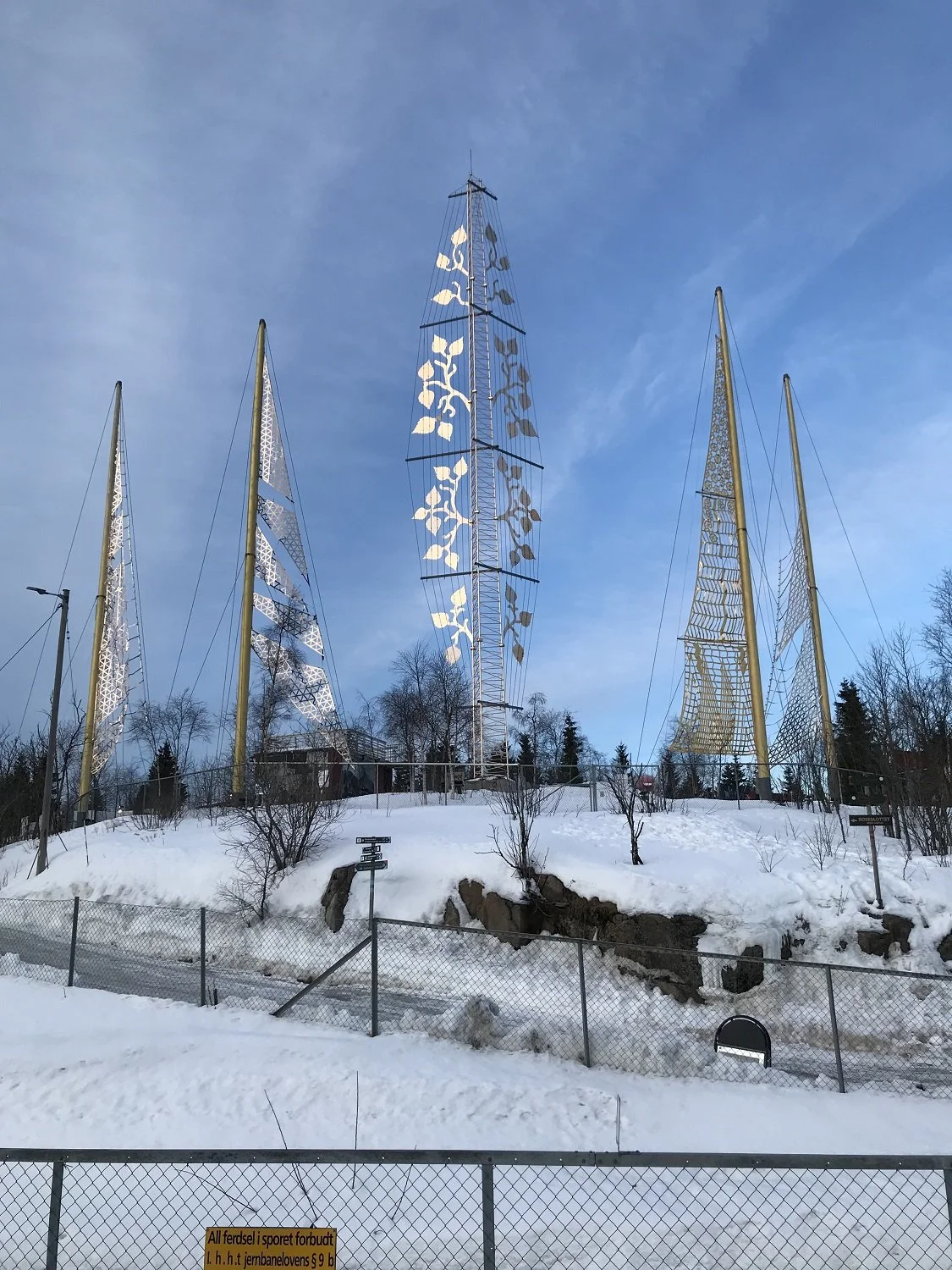 Sculpture park with metal sculptures resembling sails on a snowy hill, under a blue sky.
