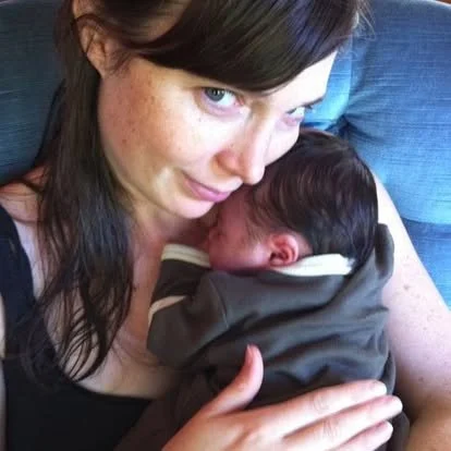 Woman holding a sleeping baby close to her chest outside.