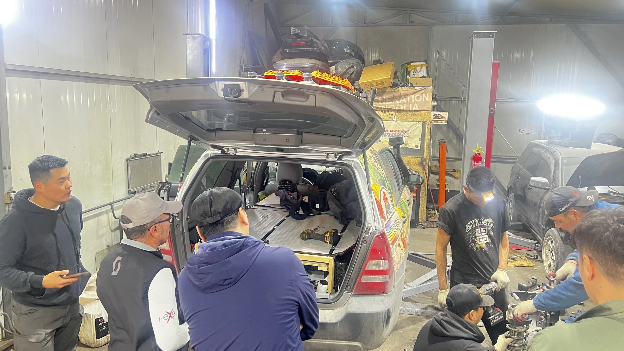 Gruppo di persone che lavora su un veicolo di emergenza in un garage, con strumenti e attrezzature intorno.