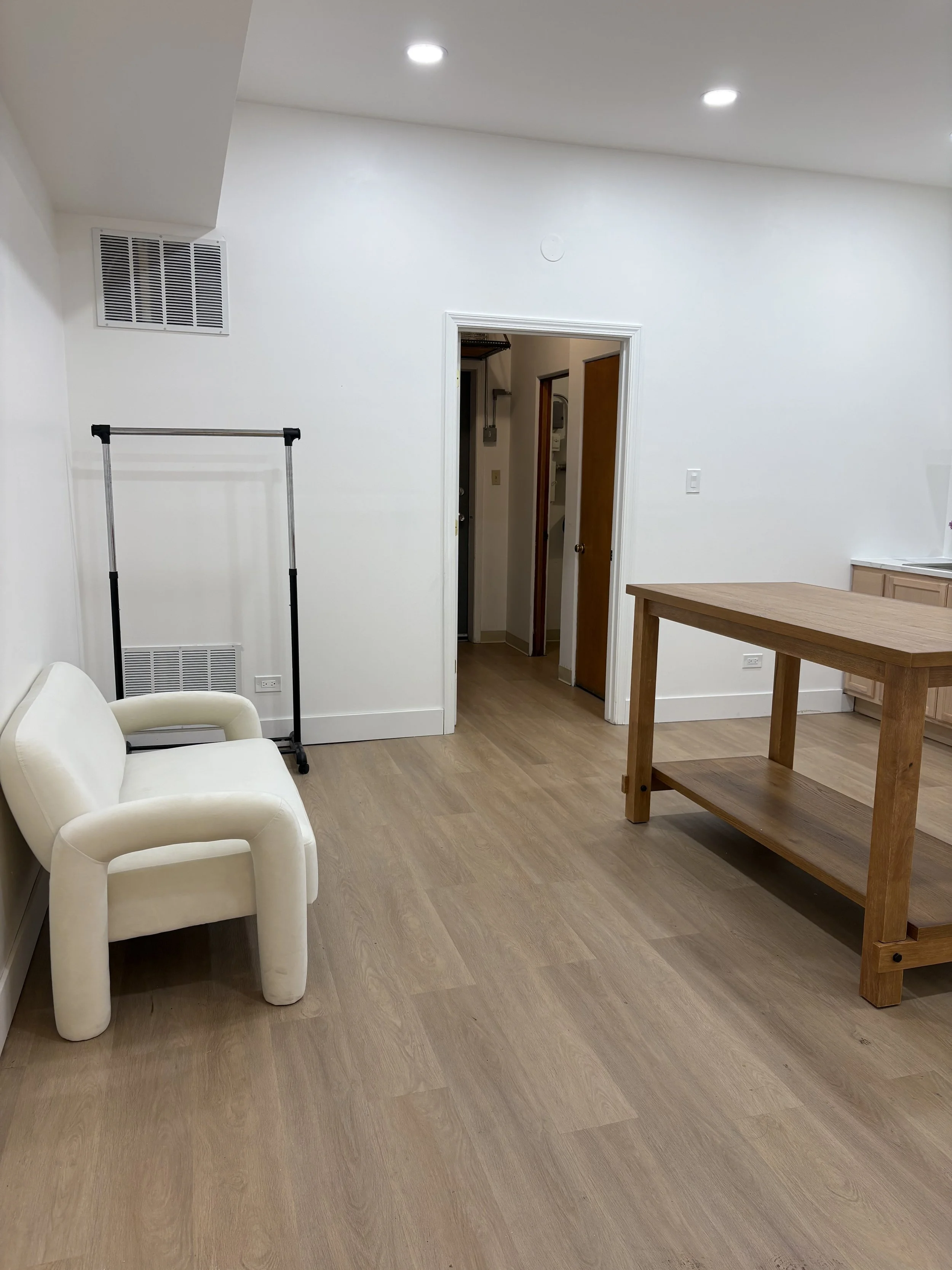 Living room with a white armchair, wooden table, and doorway leading to a hallway.