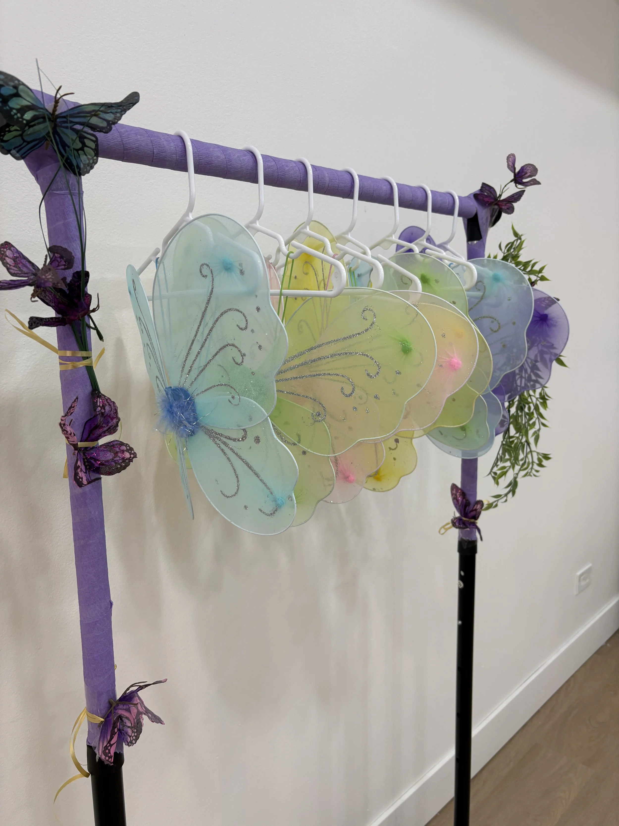 A clothing rack decorated with purple fabric and attached purple and butterfly embellishments, holding colorful butterfly-shaped wind chimes with glitter details.