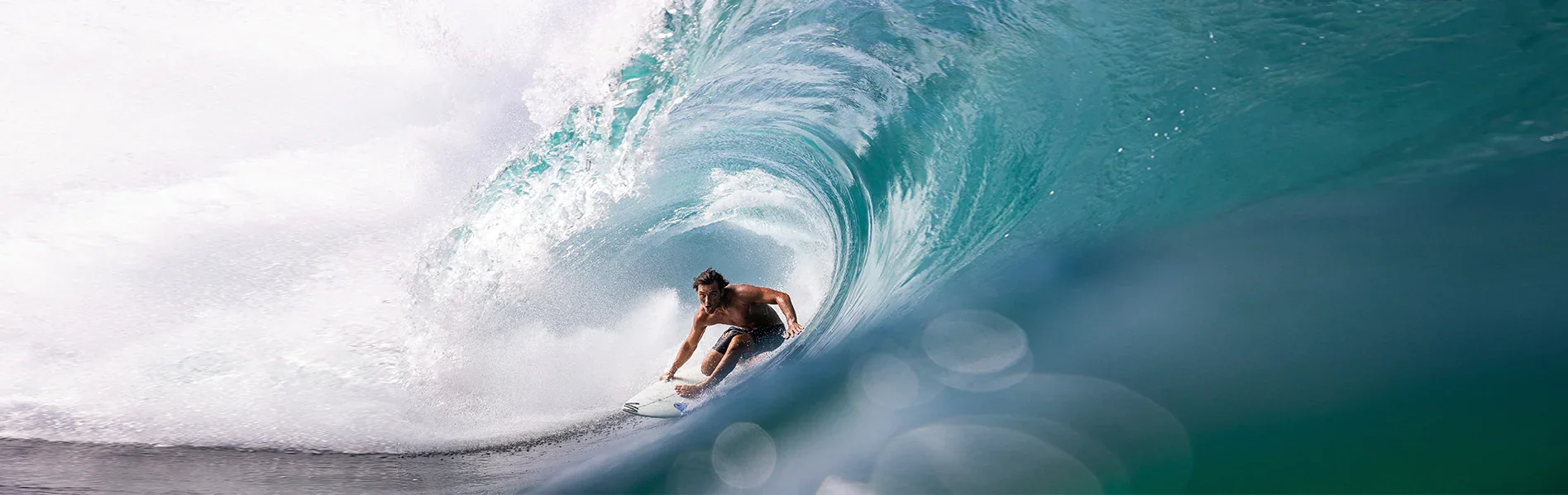 A man surfing inside a large, curling wave in the ocean.