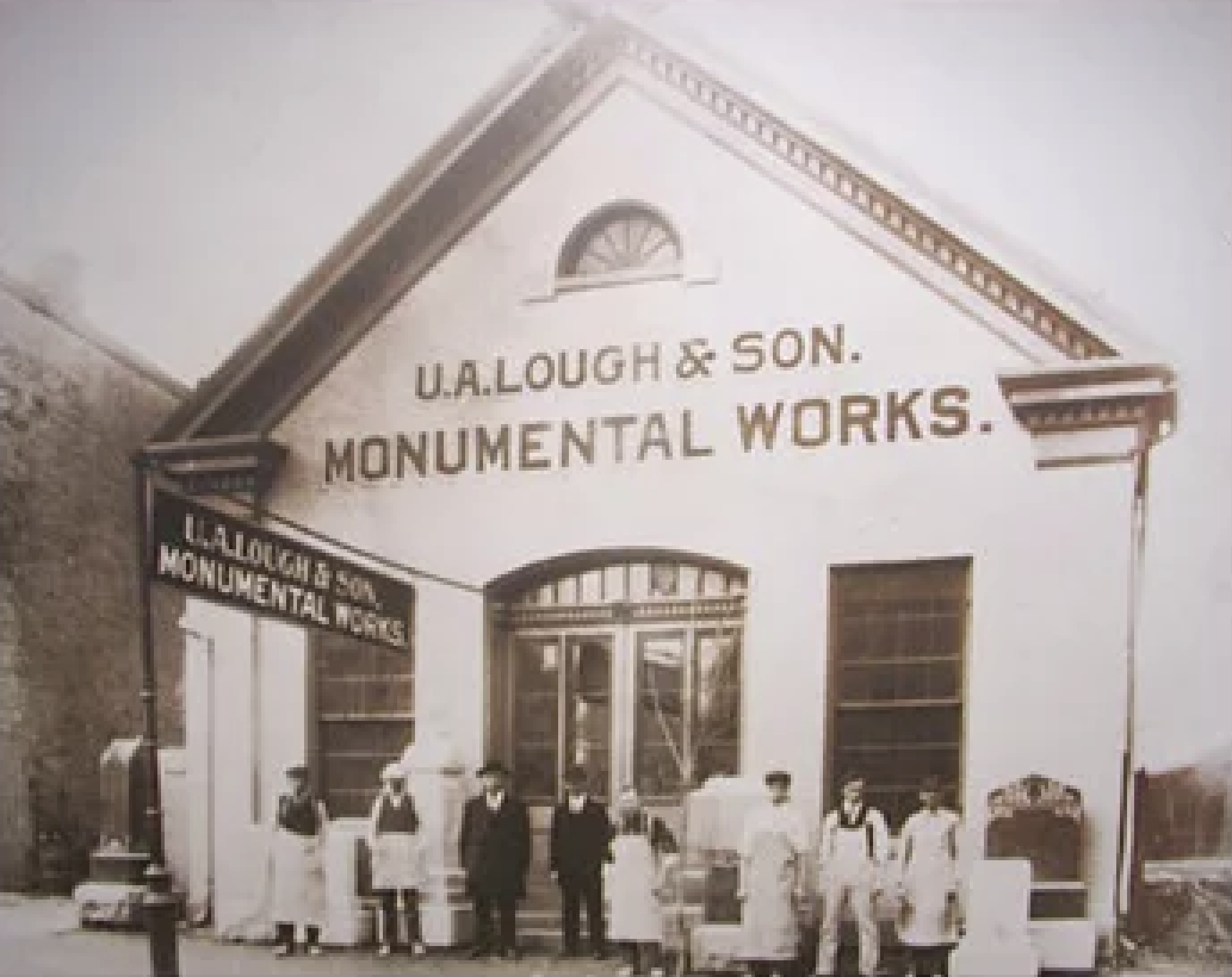 Historical black and white photograph of men lined up in front of a building labeled 'U. A. Lough & Son Monumental Works'. The men are dressed in early 20th-century clothing.