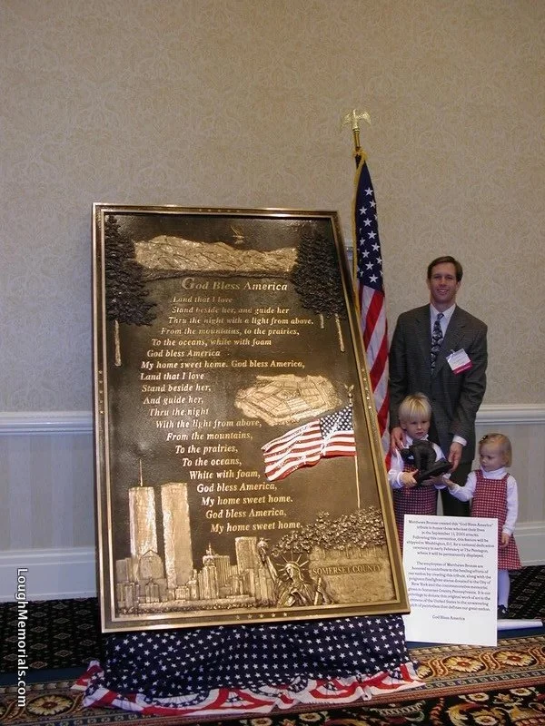 A man and two children standing next to an American flag and a memorial plaque with the American flag on it.