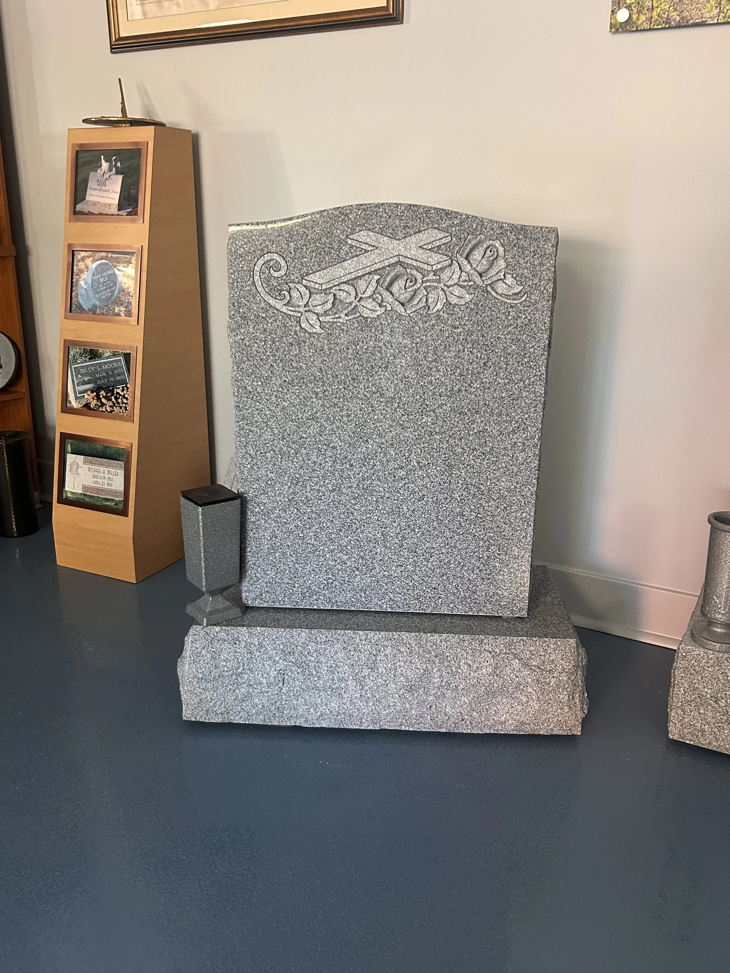 A granite memorial monument with a cross and decorative floral design engraved on the top portion, placed on a matching granite base. 