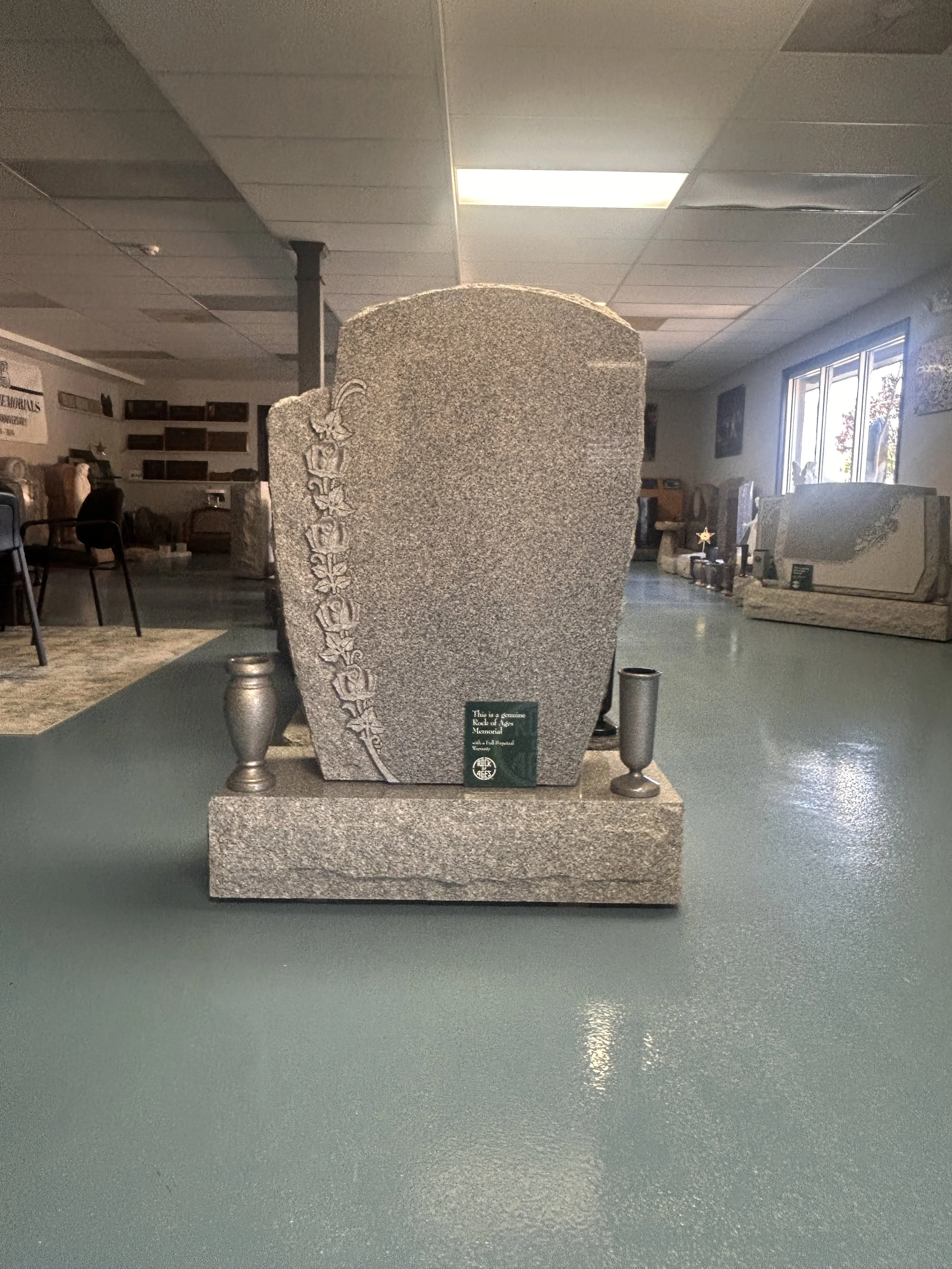 A granite headstone with a floral carving and a small plaque in front