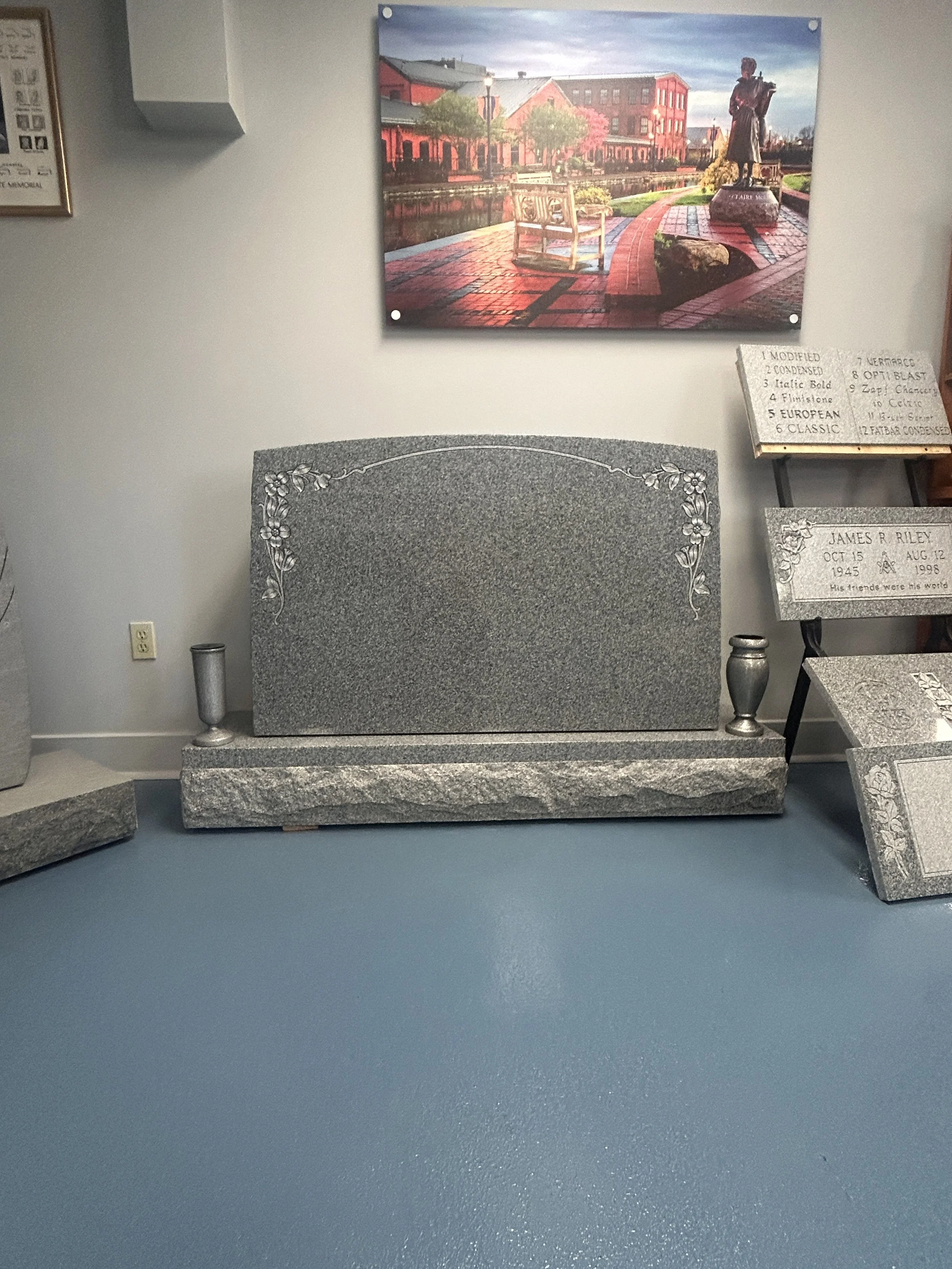 The image shows a granite headstone with engraved floral design at the top corners