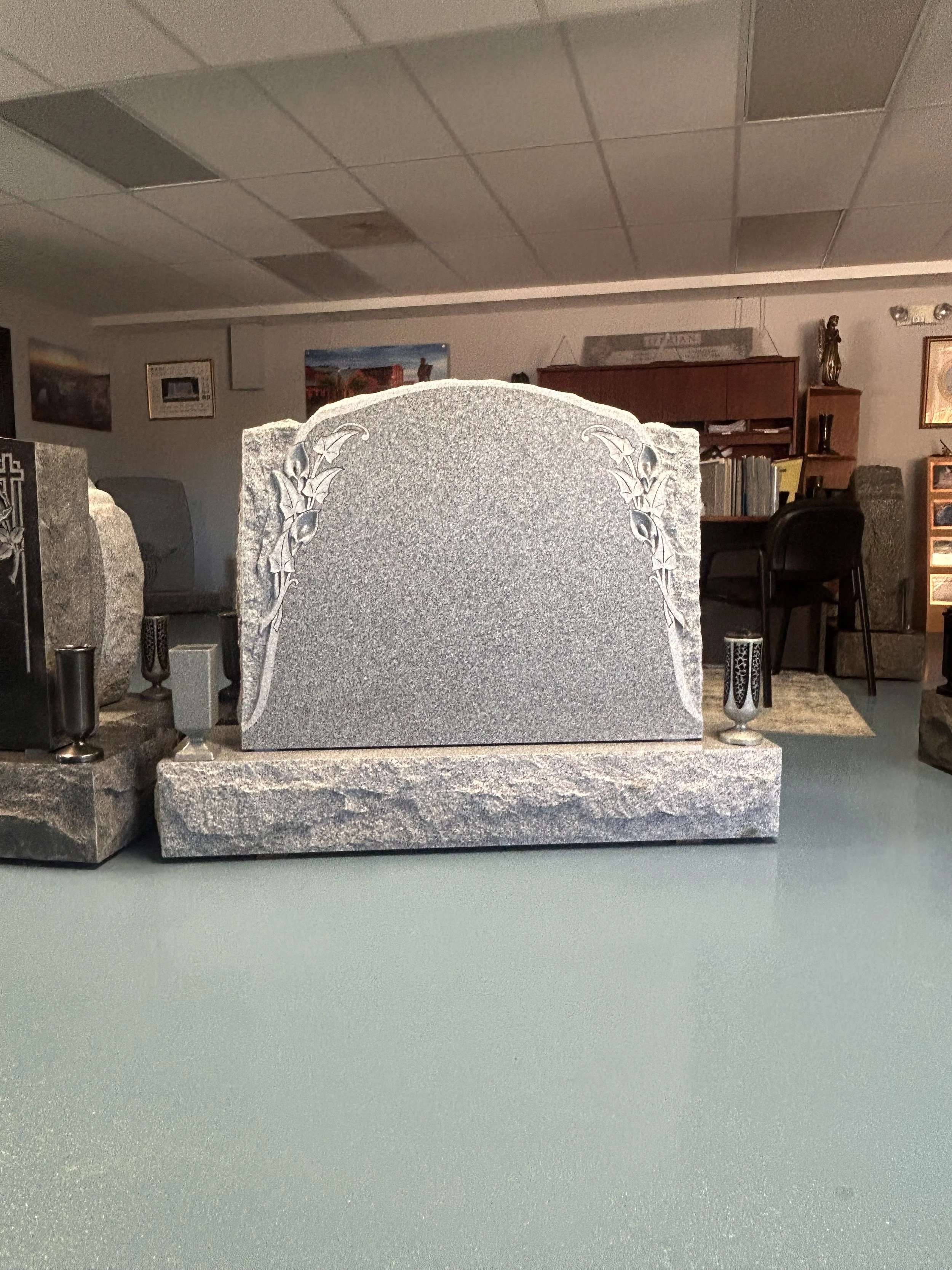 Gray granite gravestone with floral design in a room with books and artwork.