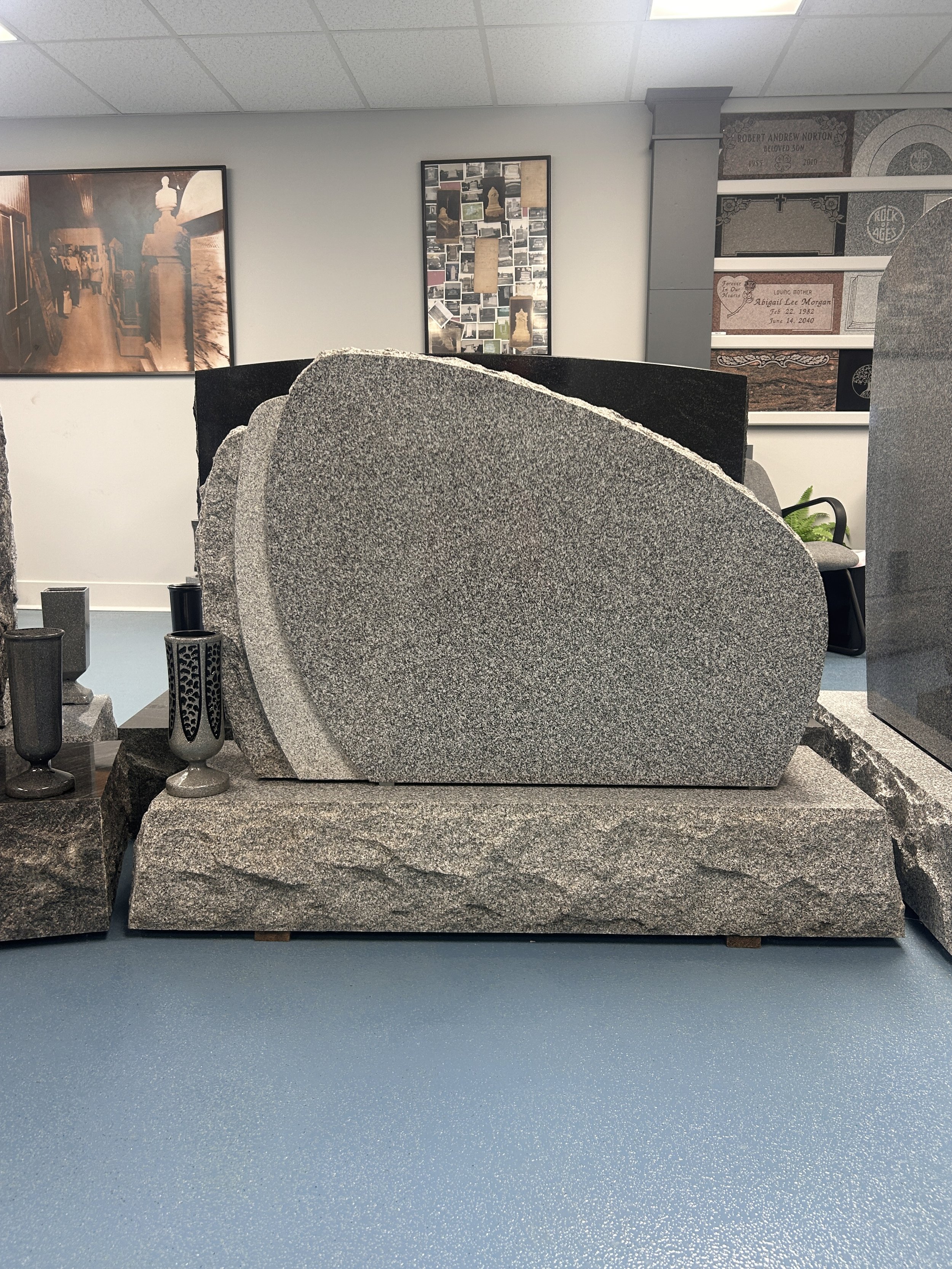 A granite monument with a curved top, resting on a matching granite base, displayed inside the Lough Memorials showroom 