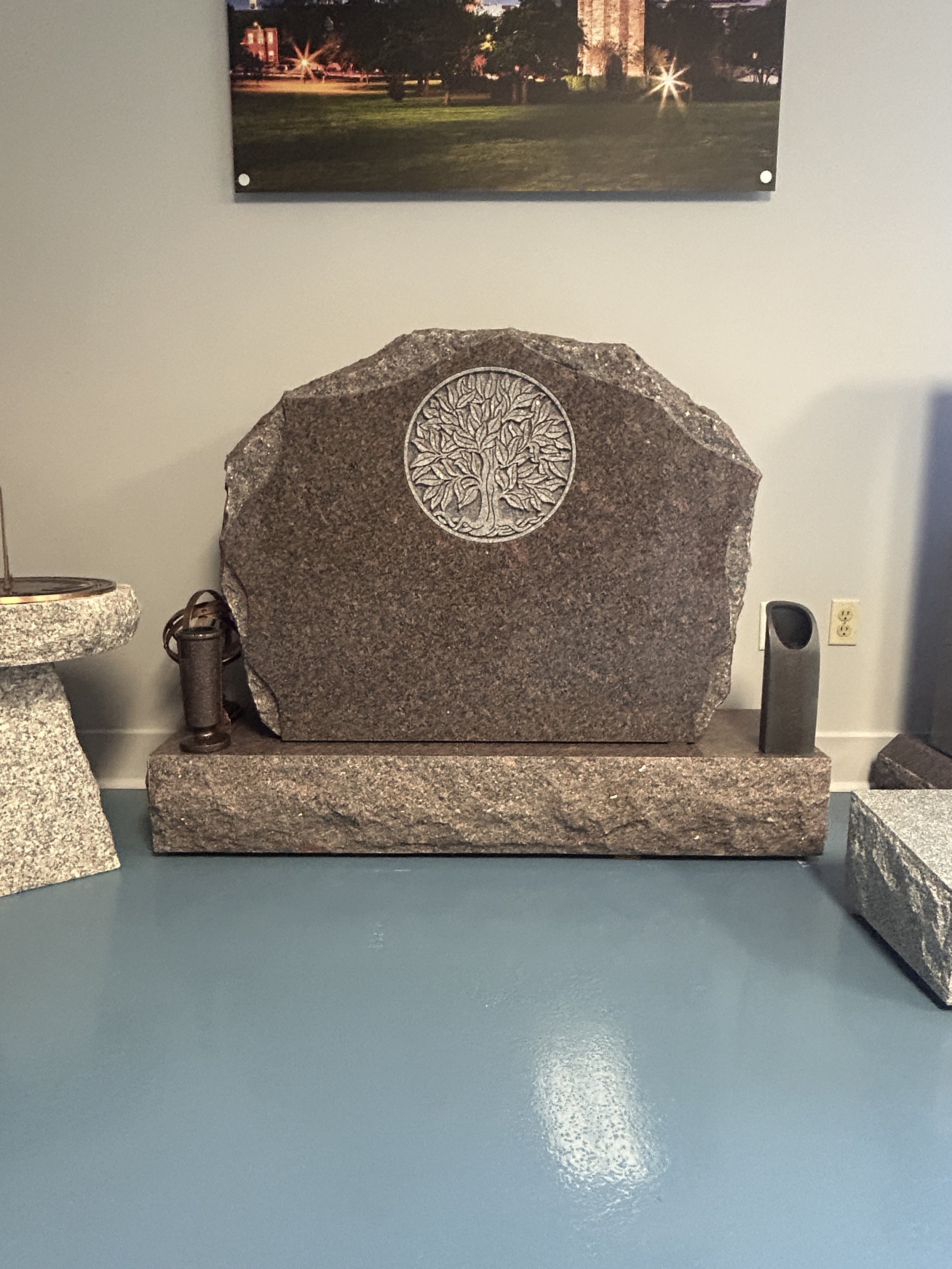 A large granite monument with a carved circular tree at the center, placed on a granite base, displayed in the Lough Memorials showroom