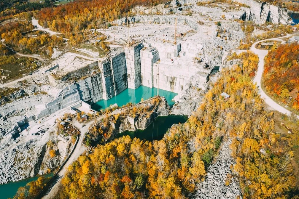 Aerial view of a large hydropower dam with water behind it, surrounded by autumn-colored trees and roads.