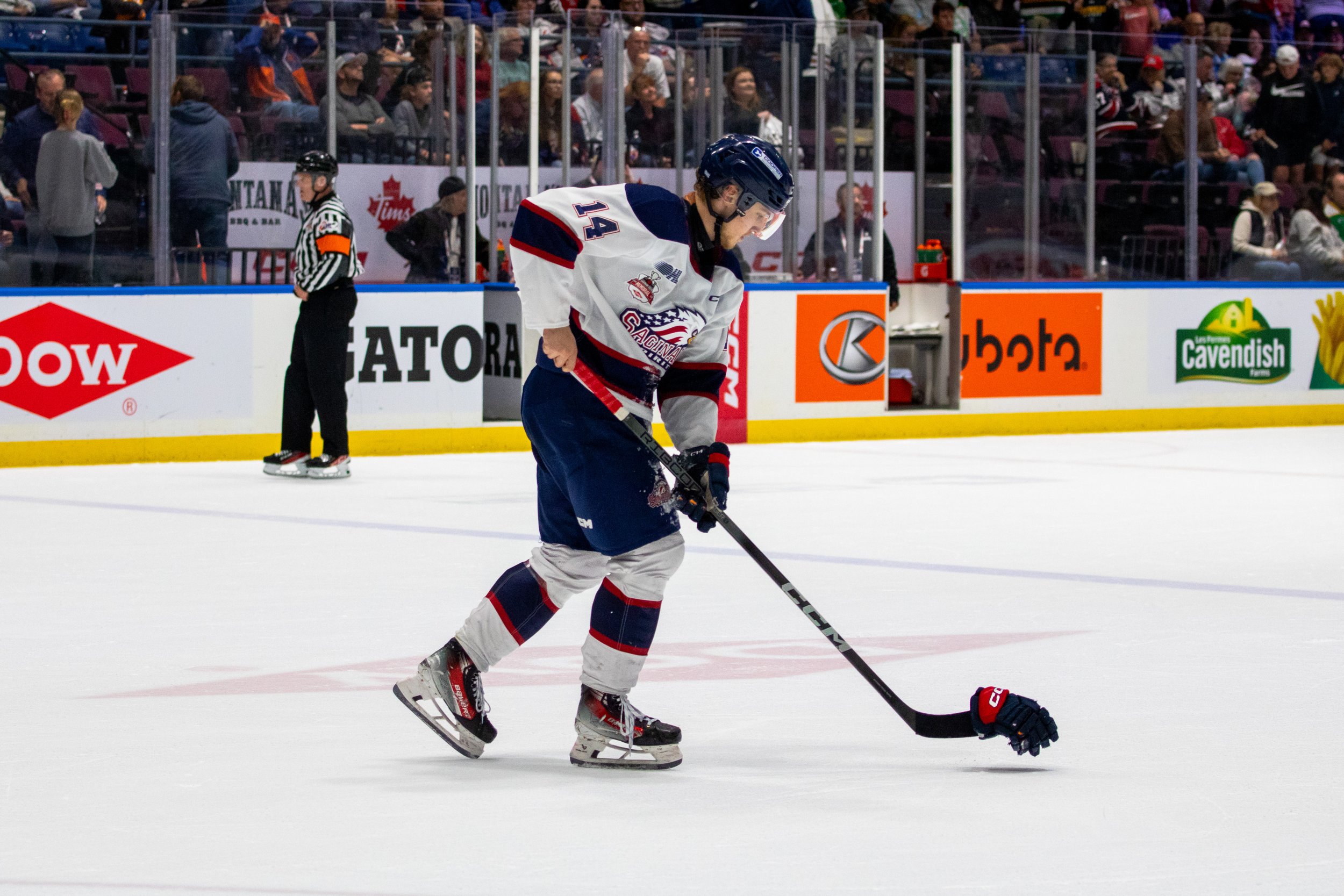 Hockey player on ice rink preparing to hit the puck, with spectators in the background.