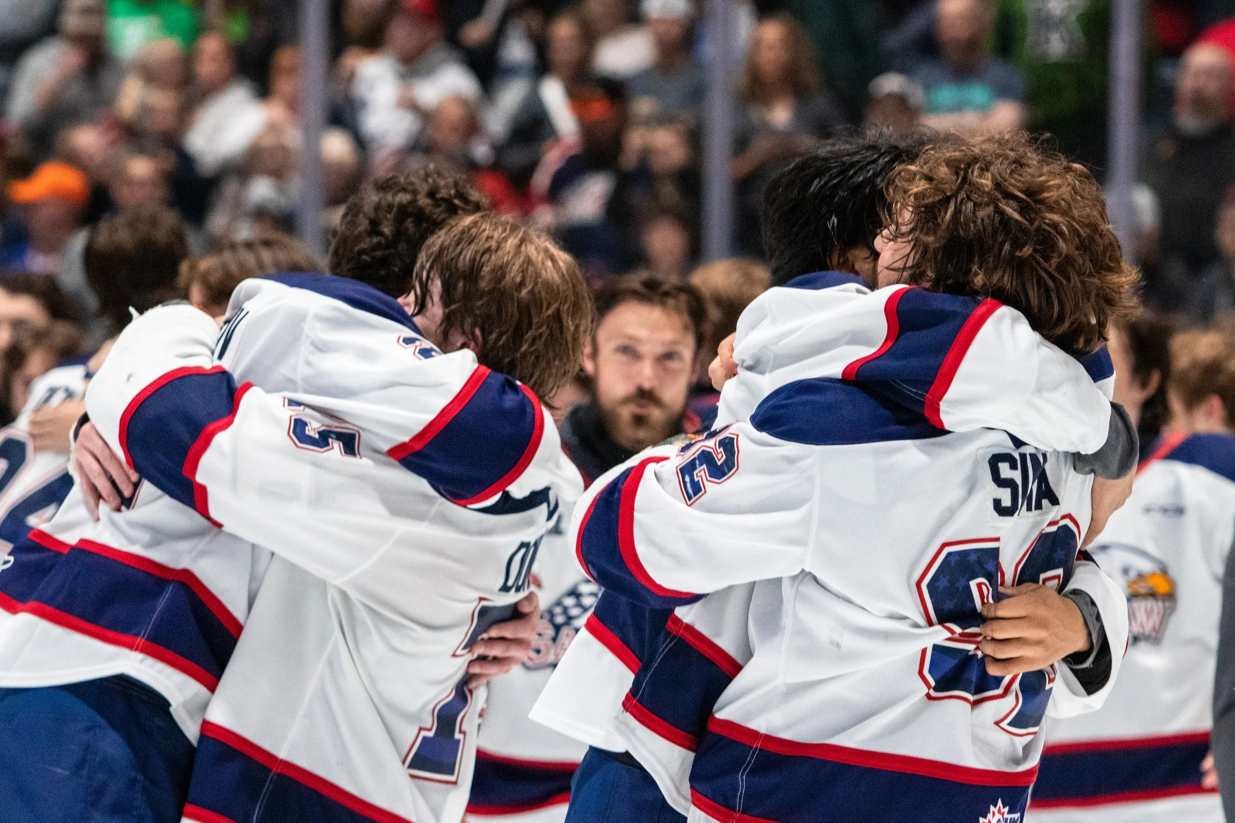 Hockey players in team jerseys hugging each other during a game or event.