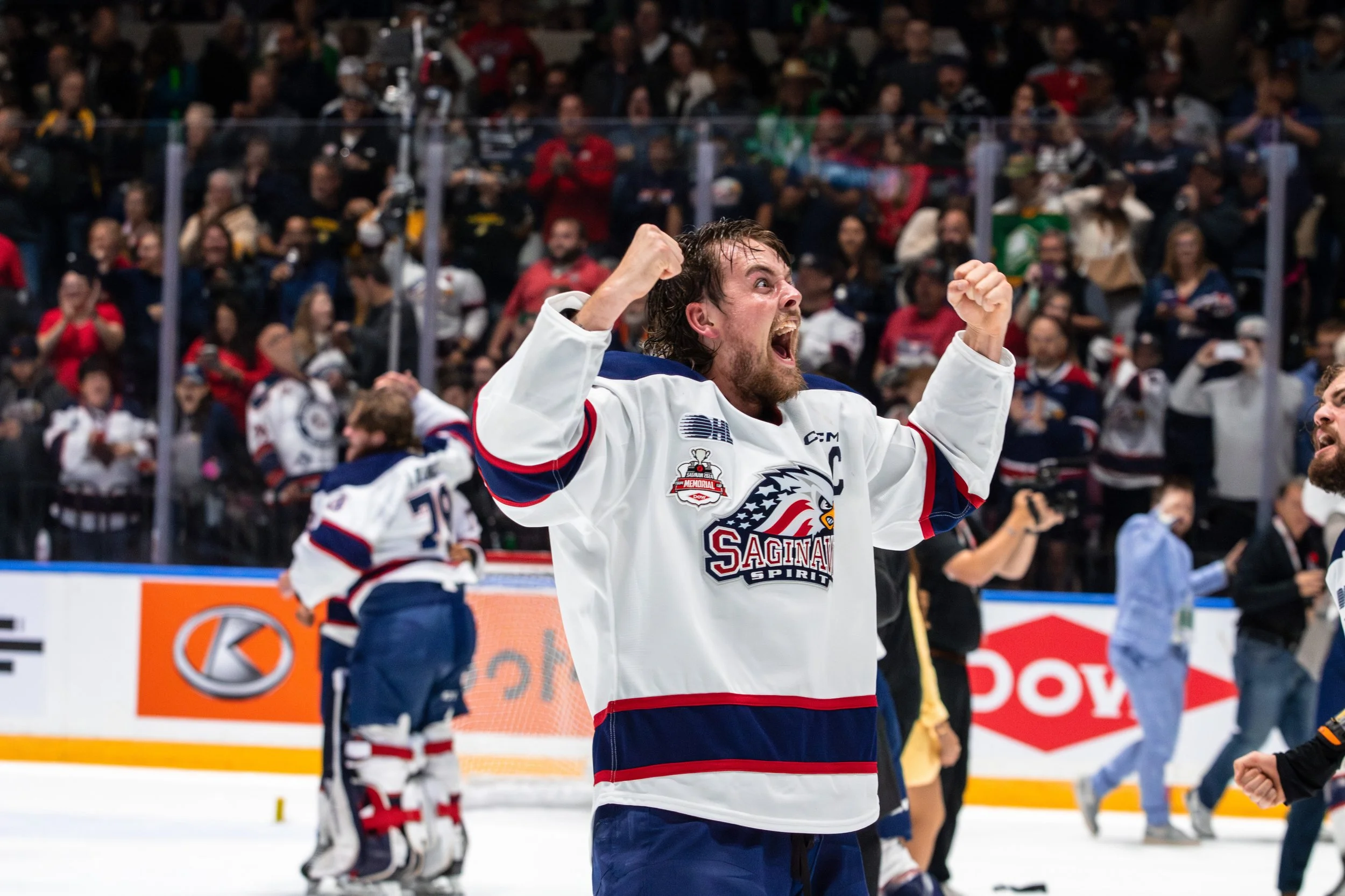 Hockey player celebrating victory on ice rink, wearing Saginaw Spirit jersey, with fans in the background.