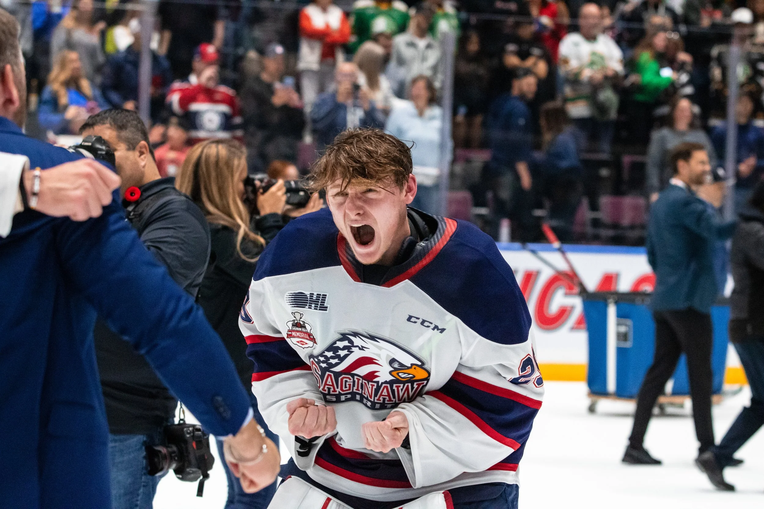 Hockey player in Saginaw Spirit jersey celebrates passionately, clenched fists, shouting with intense emotion on the ice during a game.