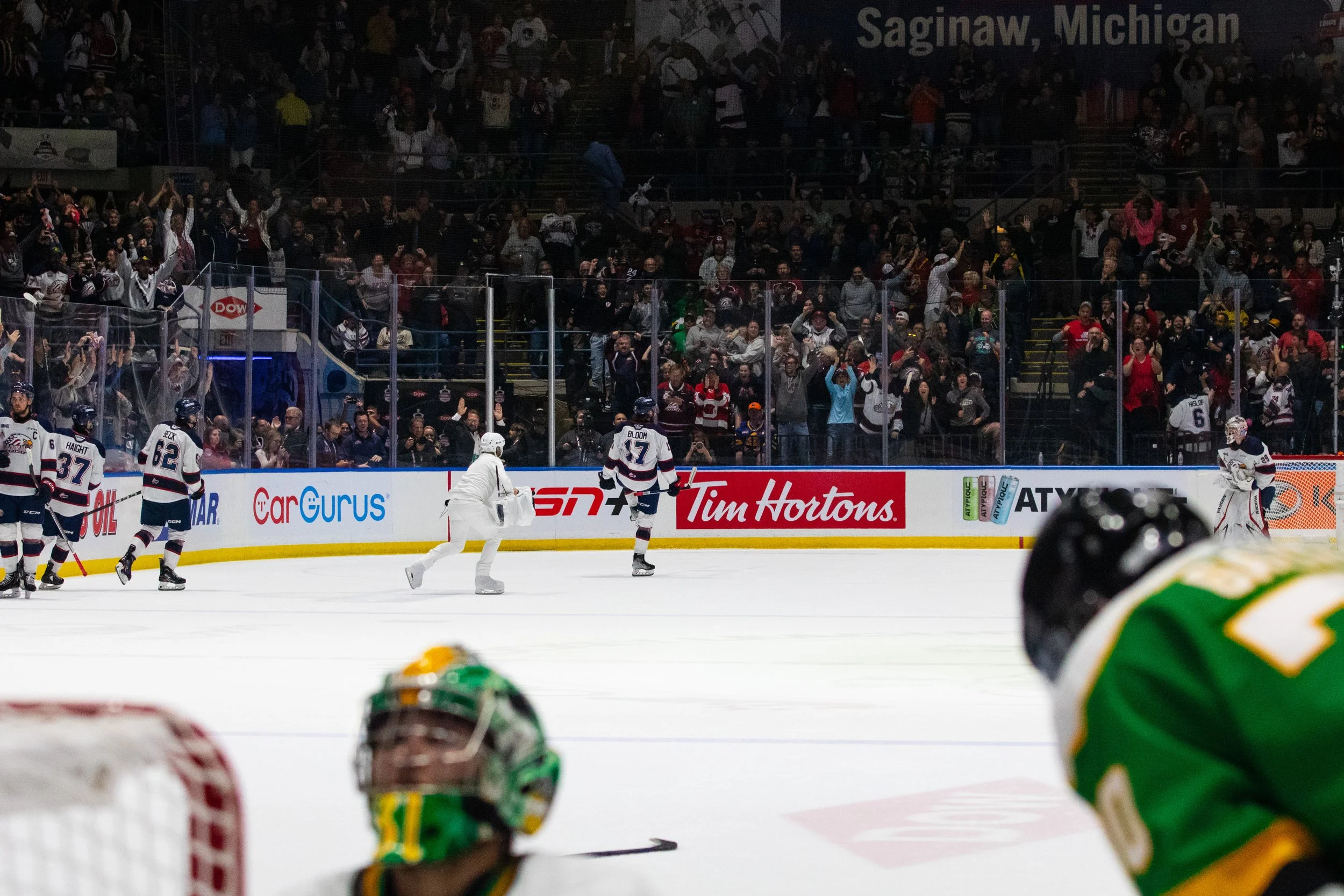 Ice hockey game with players on the ice and cheering fans in the stands at Saginaw, Michigan.