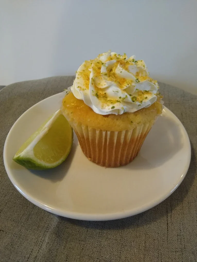 Lemon cupcake with whipped frosting and lime wedge on a white plate.