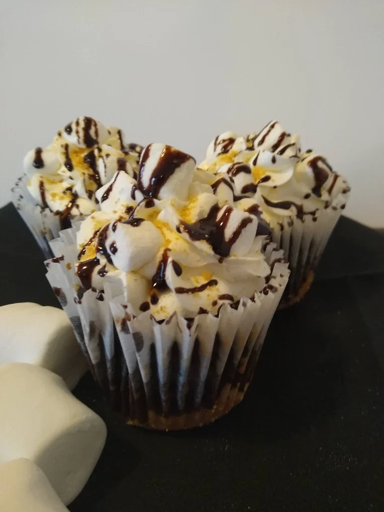 Two cupcakes topped with whipped cream, chocolate drizzle, and yellow sprinkles, placed on a black surface