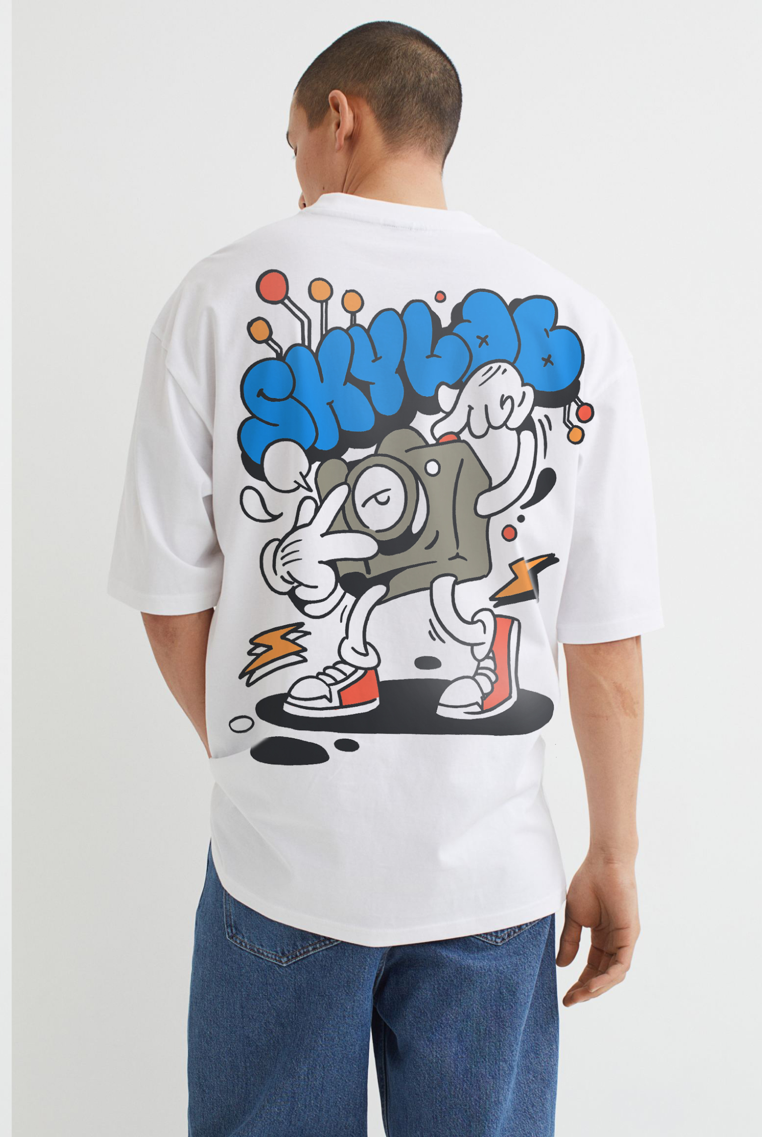 Back of a person wearing a white T-shirt with a graffiti-style cartoon character holding a camera and making a peace sign, surrounded by colorful abstract designs.