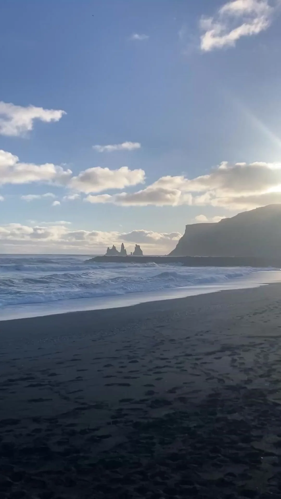 Black sand and sneaker waves with stone columns in the distance at Black Sand beach in Iceland.