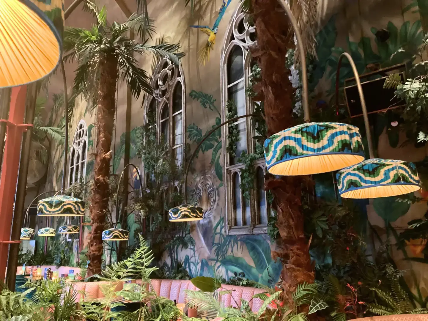 Tropical restaurant interior with palm trees, jungle murals, and colourful hanging lamps in Breda, Netherlands.