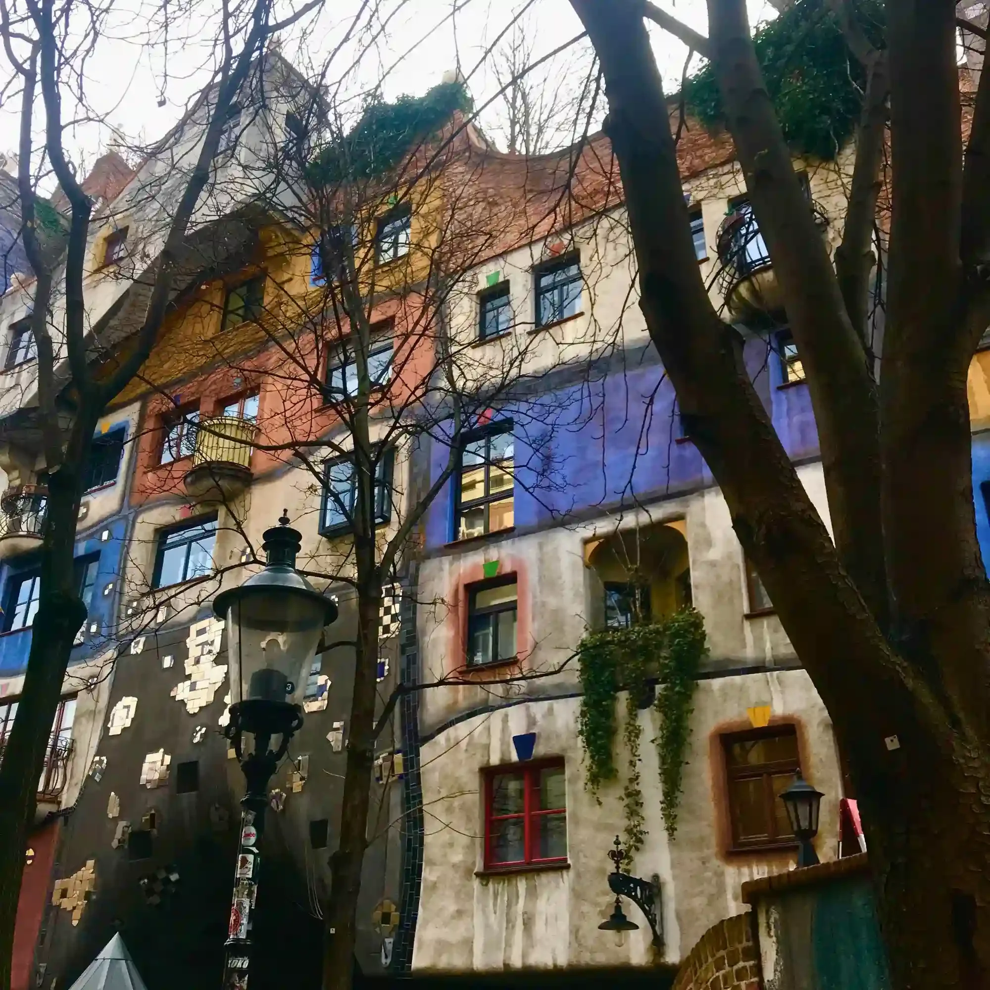 Colourful Hundertwasserhaus apartments in Vienna framed by bare trees and whimsical curved architecture.