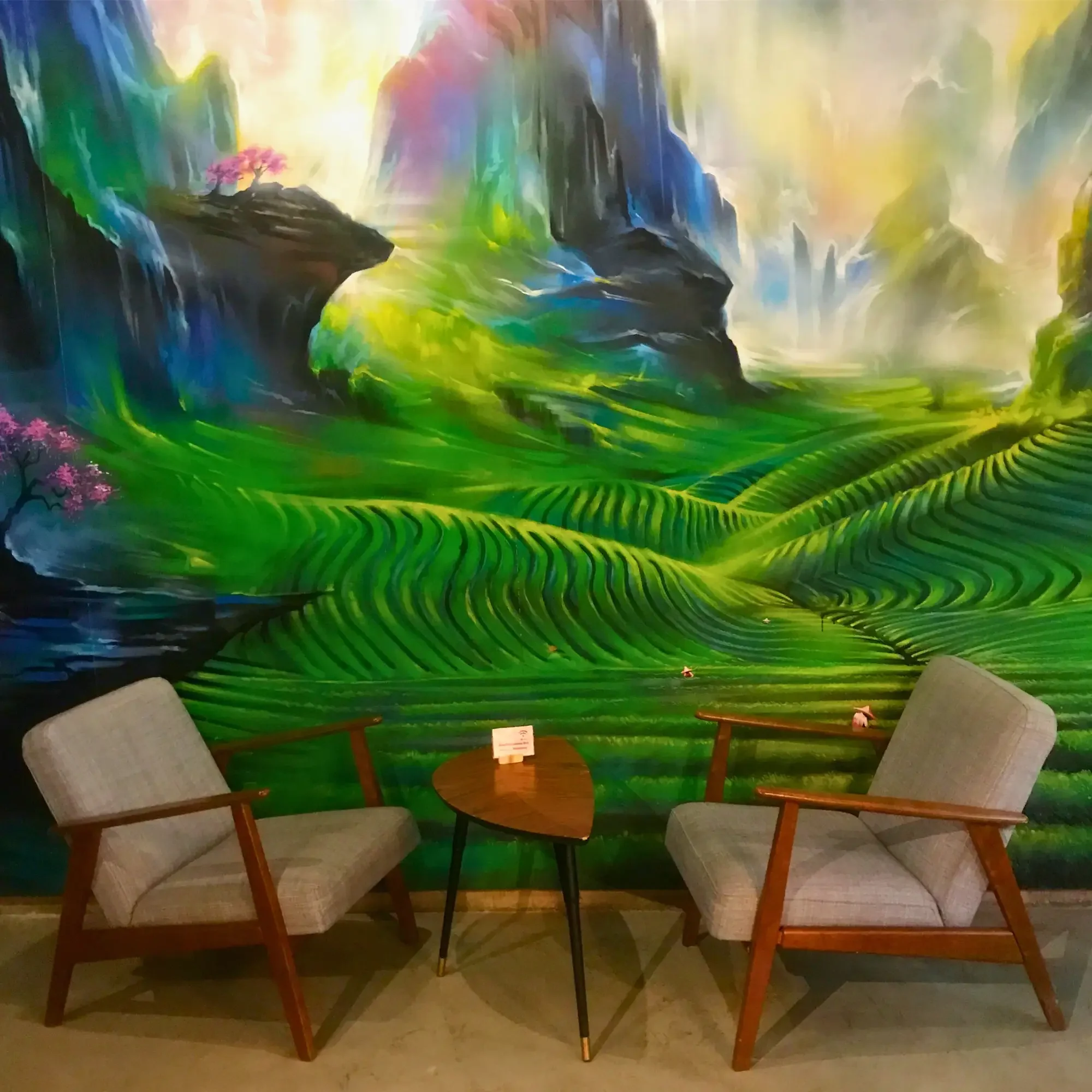 Mid-century chairs sit beneath a vivid green landscape mural inside a modern café with nature-inspired décor.