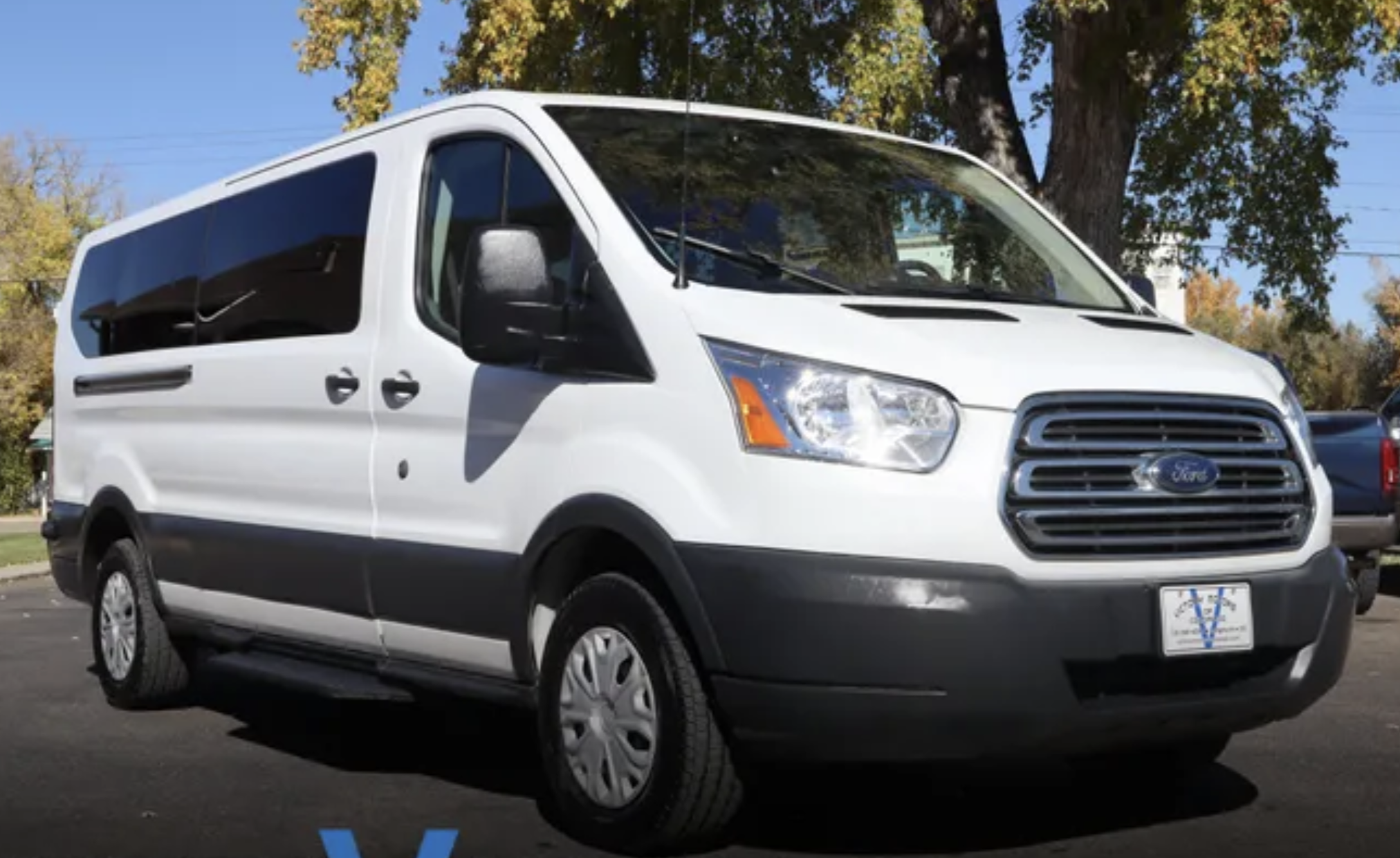 A white Ford Transit van parked in a lot with trees and clear blue sky in the background.