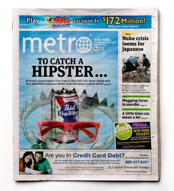 Front page of a Metro newspaper with headline 'TO CATCH A HIPSTER...' featuring an image of a red pair of sunglasses and a can of Pabst Blue Ribbon beer. Additional headlines include 'Nuke crisis looms for Japanese,' 'Mugging turns to murder,' and an advertisement for winning free tickets.