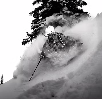 A skier in winter gear skiing through deep snow in a snowy landscape with trees in the background.