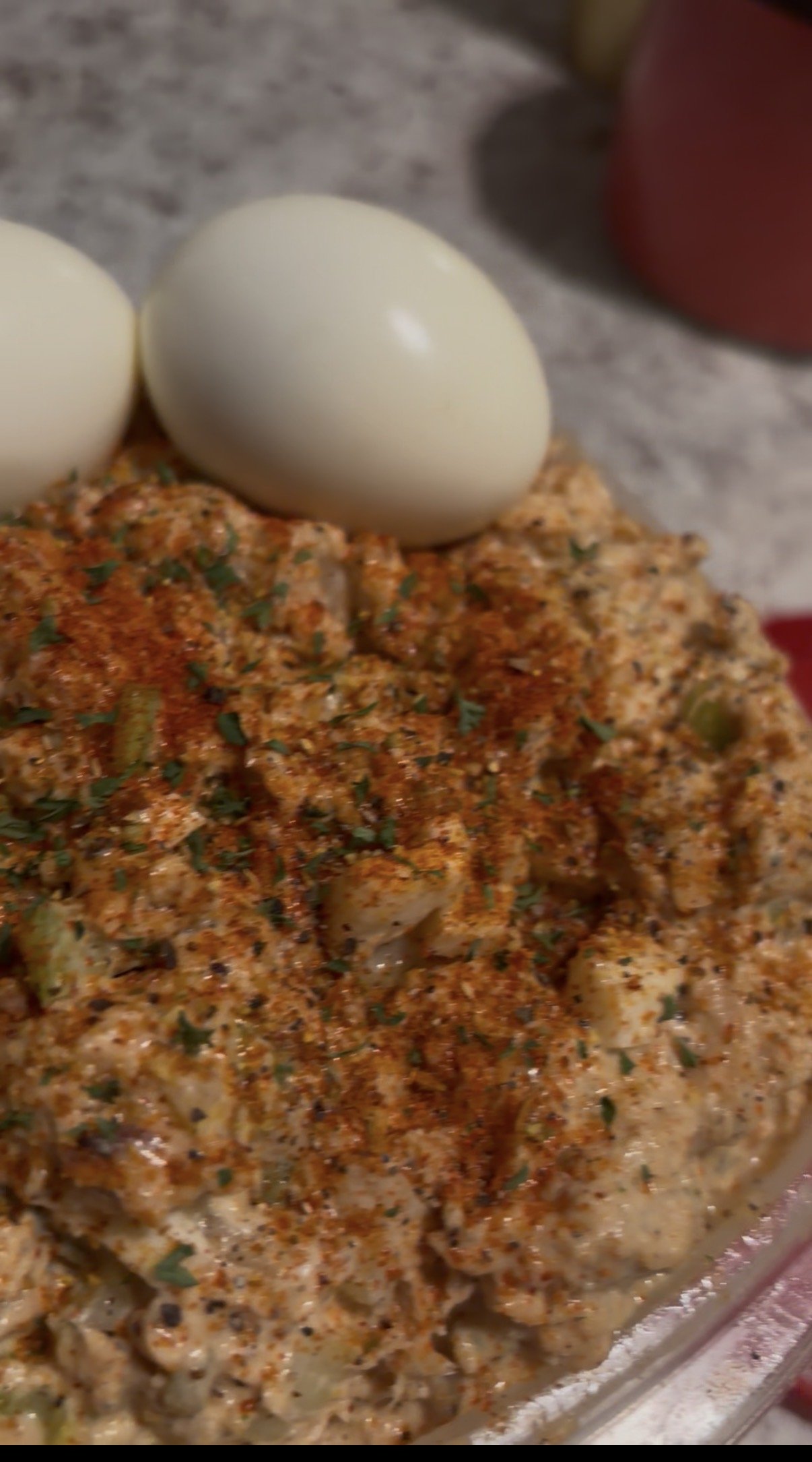 Close-up of a seasoned dish topped with herbs, two peeled boiled eggs, on a kitchen counter.