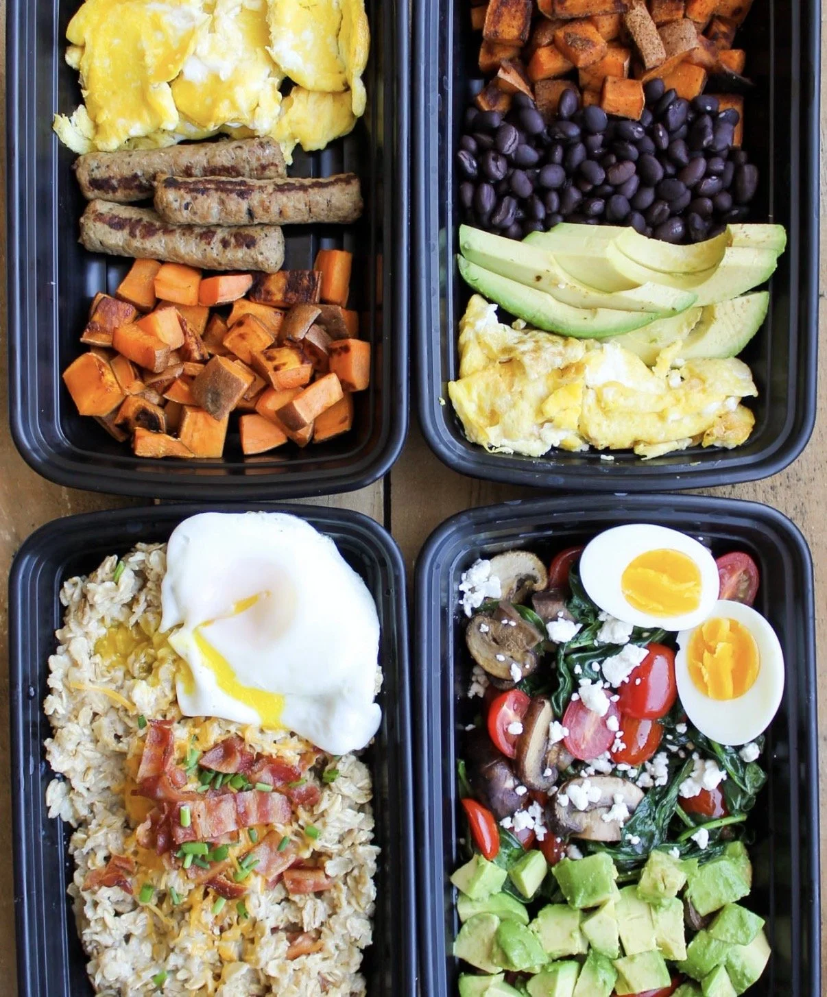 Four meal prep containers filled with breakfast and lunch foods including scrambled eggs, sweet potato hash, sausage links, avocado slices, black beans, cherry tomatoes, mushrooms, spinach, hard-boiled eggs, and rice with bacon.