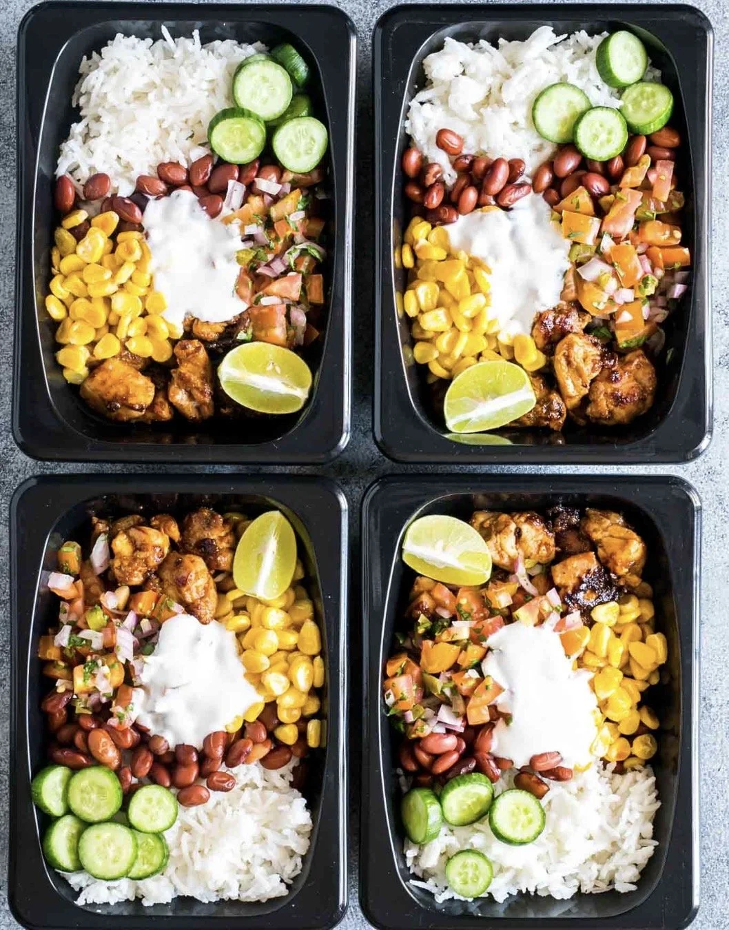 Four meal prep containers with rice, cucumber slices, kidney beans, corn, diced tomatoes, grilled chicken pieces, and lime wedges, with some containers also containing sour cream.