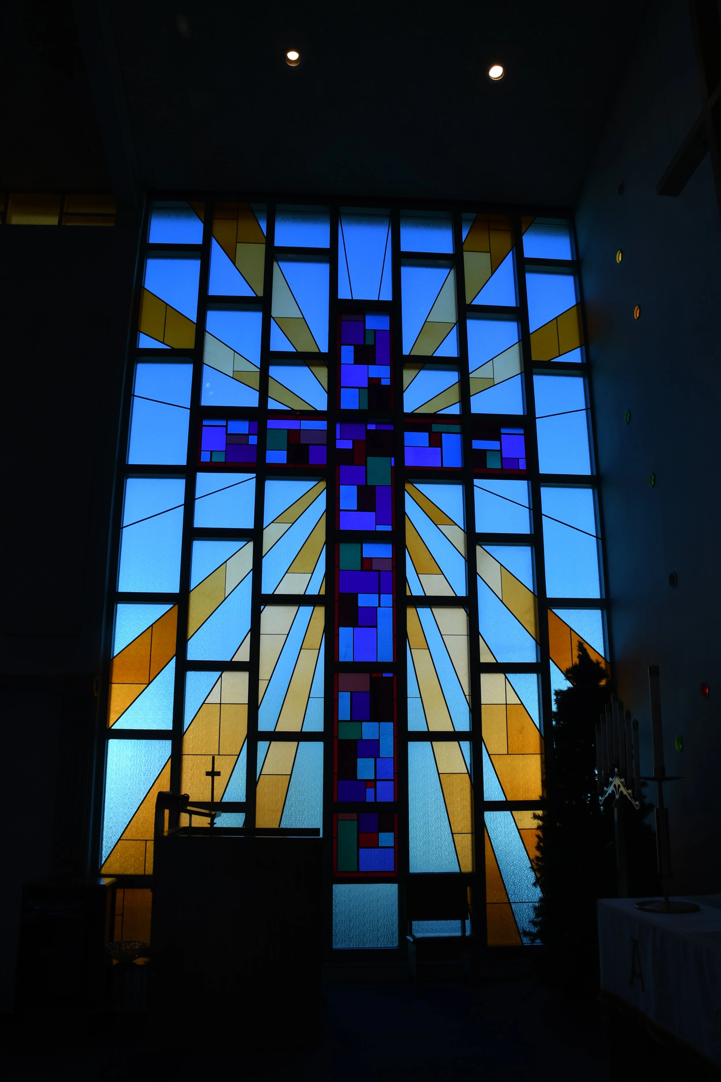 A colorful stained glass window depicting a cross with rays of light spreading outward, inside a church.