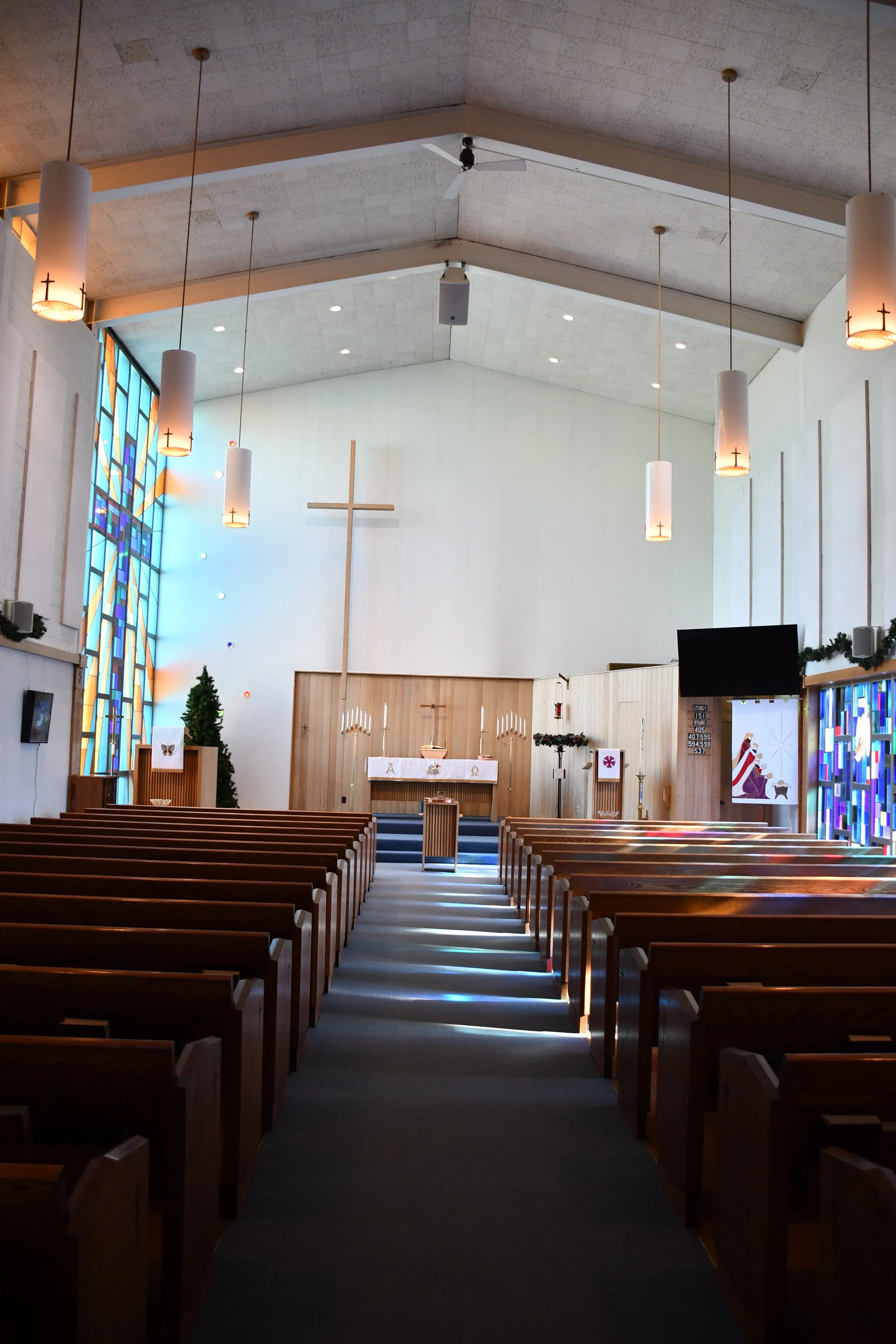 Interior of a church with pews, altar, and a large cross on the wall, decorated for Christmas with candles, Christmas trees, and festive decorations.