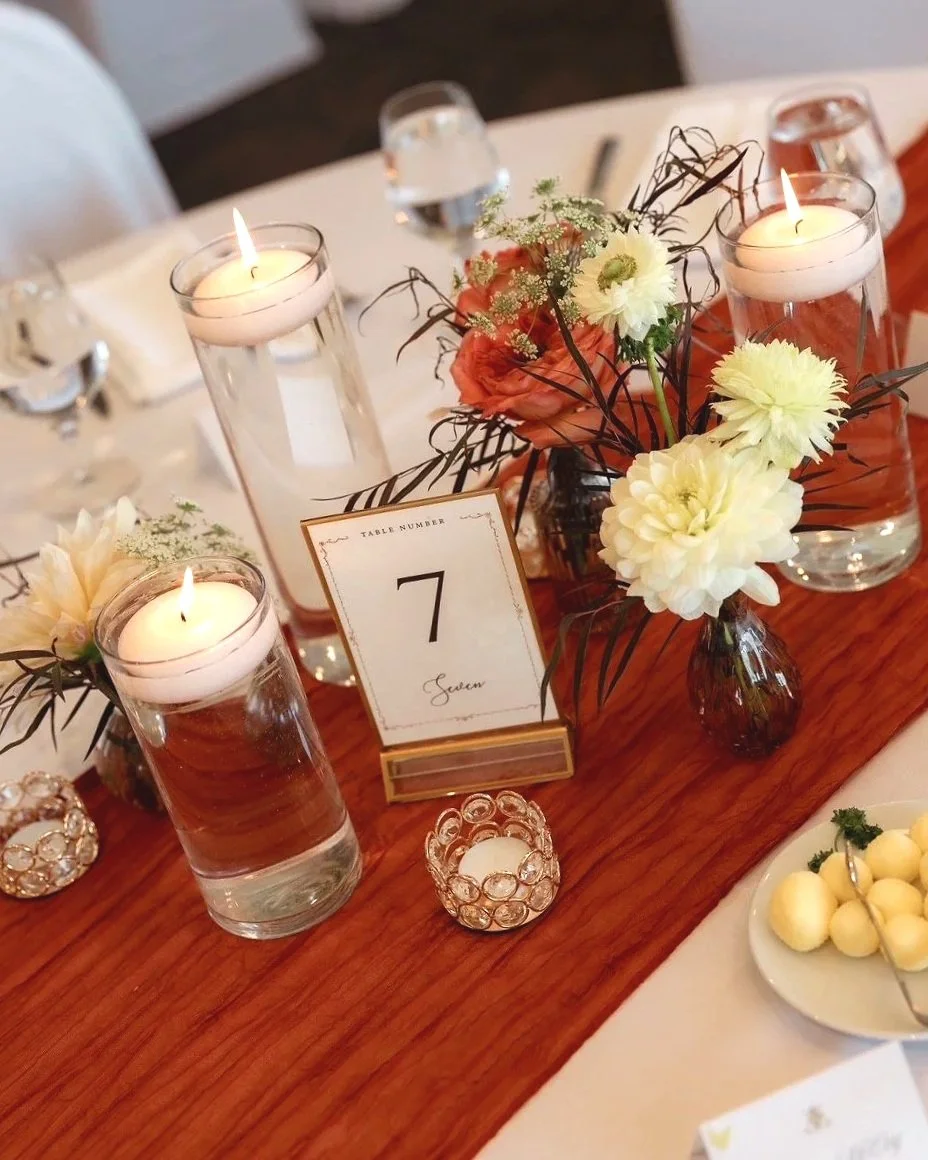 A table decorated with flowers in vases, candles in glass holders, and a table number sign indicating '7'.