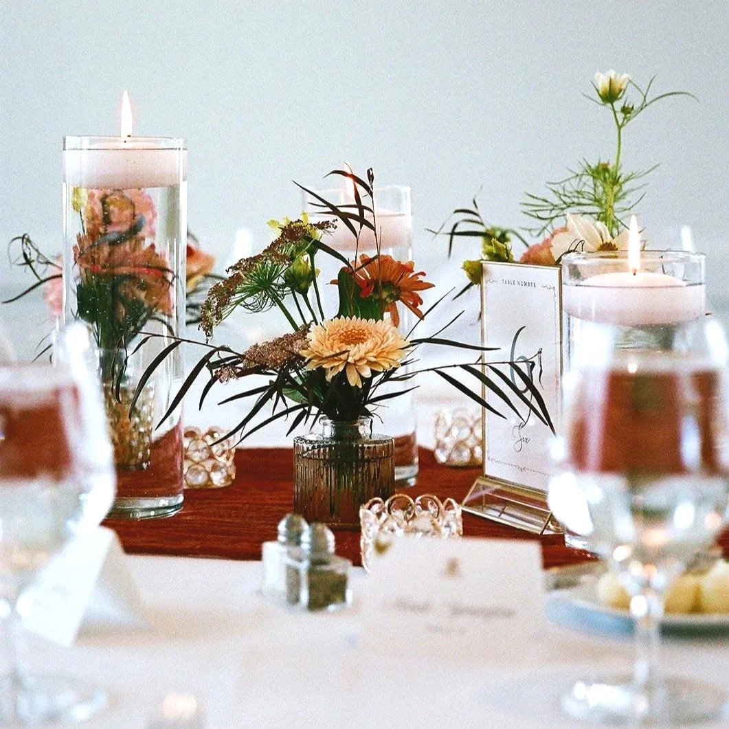 Decorative table setting featuring floral arrangements in glass vases, candles, and table cards.