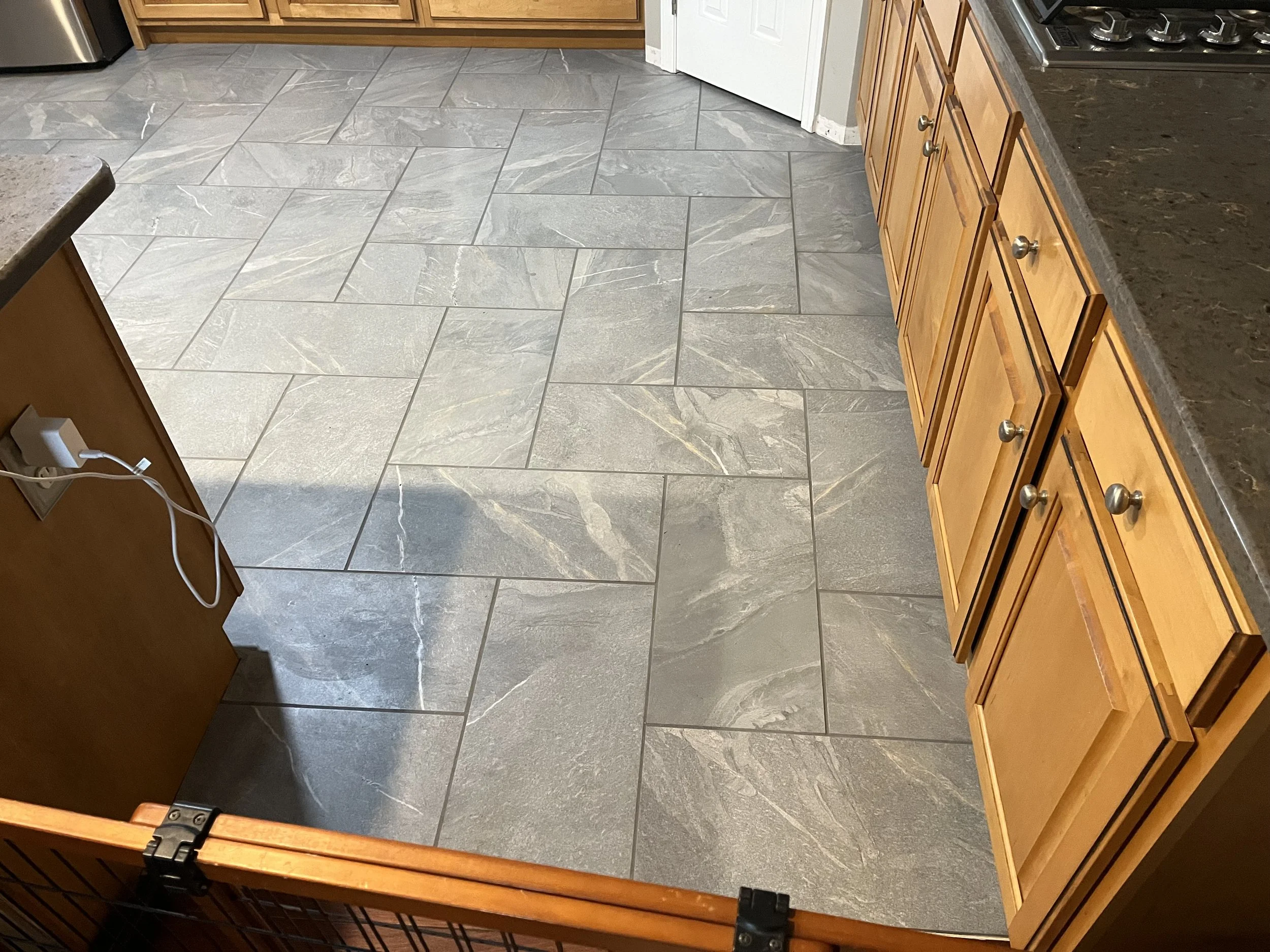 Kitchen floor with large gray stone tiles, wooden cabinets, and a gray countertop.