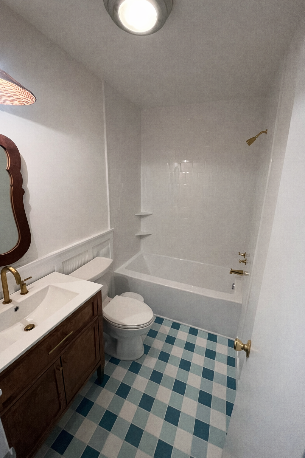 Bathroom with white walls, a wooden vanity with a white sink, a mirror, a toilet, a bathtub with gold fixtures, and a blue and white checkered floor.