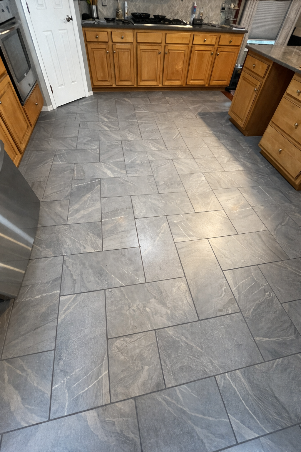 Kitchen with wooden cabinets, gray tile flooring, and stainless steel appliances.