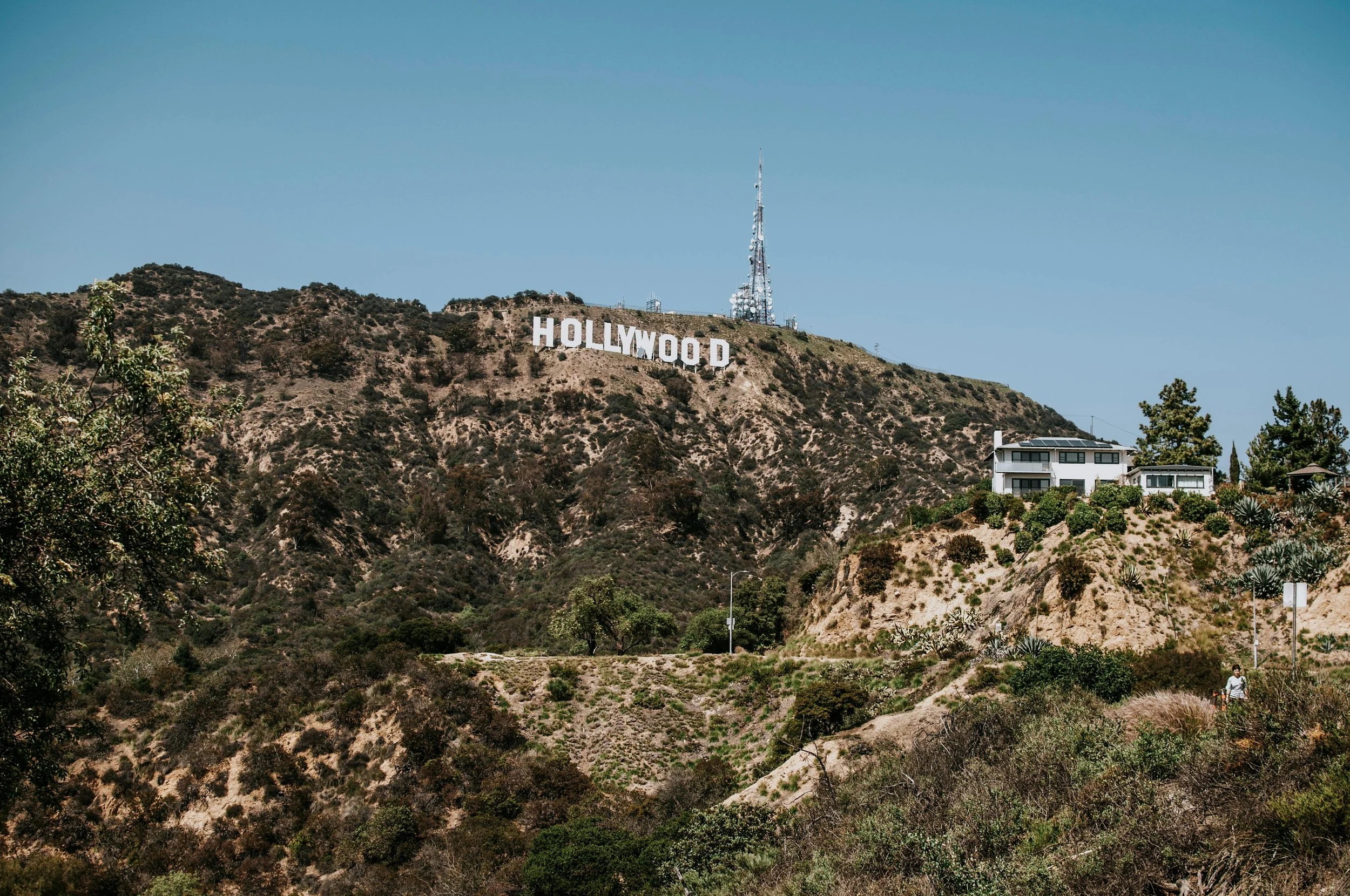 The Hollywood sign on a hillside with houses and trees in the foreground and a clear blue sky above.