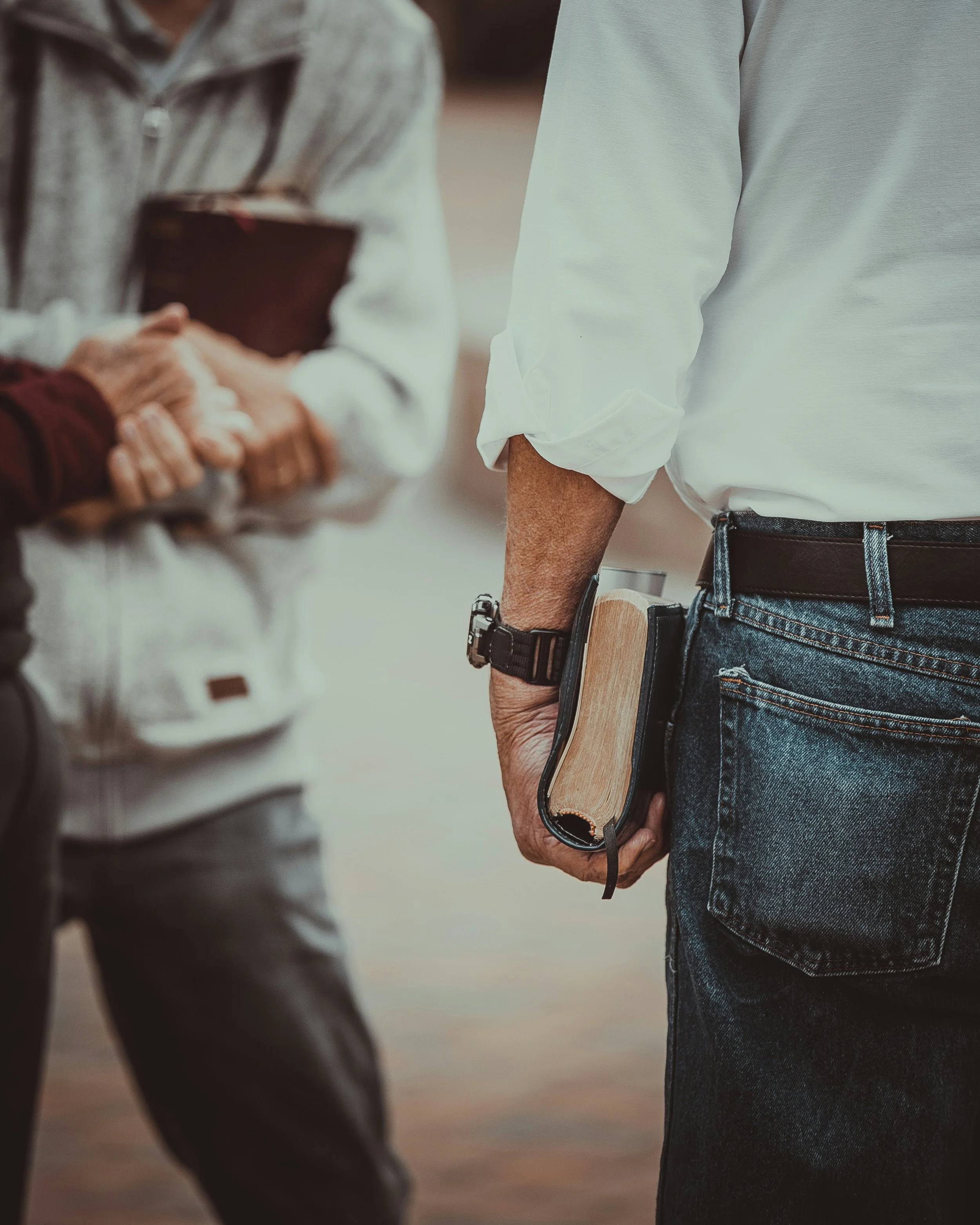 Three people stand in a circle, two holding bibles as they share conversations about faith and scripture