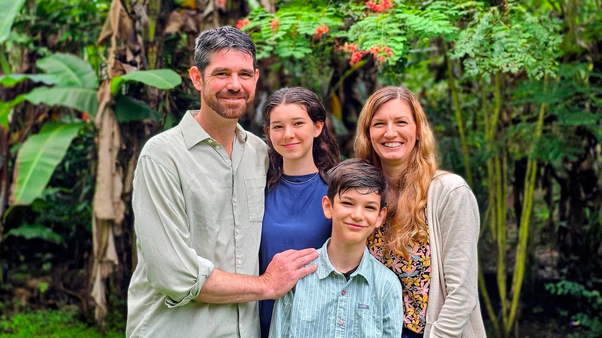 Family of five standing outdoors in a lush green garden, smiling at the camera.