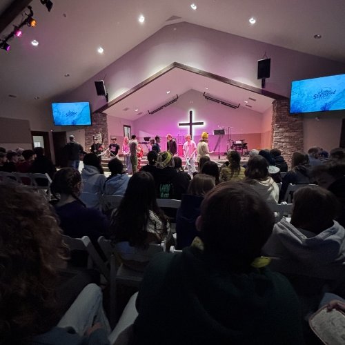 Church service with people seated, stage with musicians, cross symbol, and two large screens on the walls.