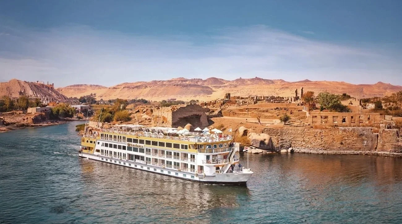 A luxury Sanctuary riverboat cruising the Nile River in Egypt, passing ancient temple ruins and desert landscapes.